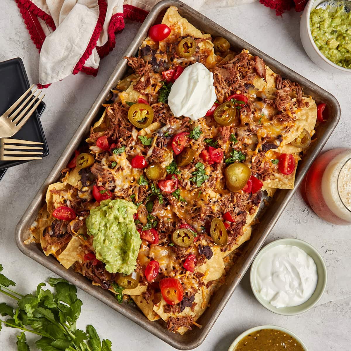 nachos with pulled pork, refried beans, cheese, sour cream, guacamole, tomatoes, and jalapenos on a sheet pan.