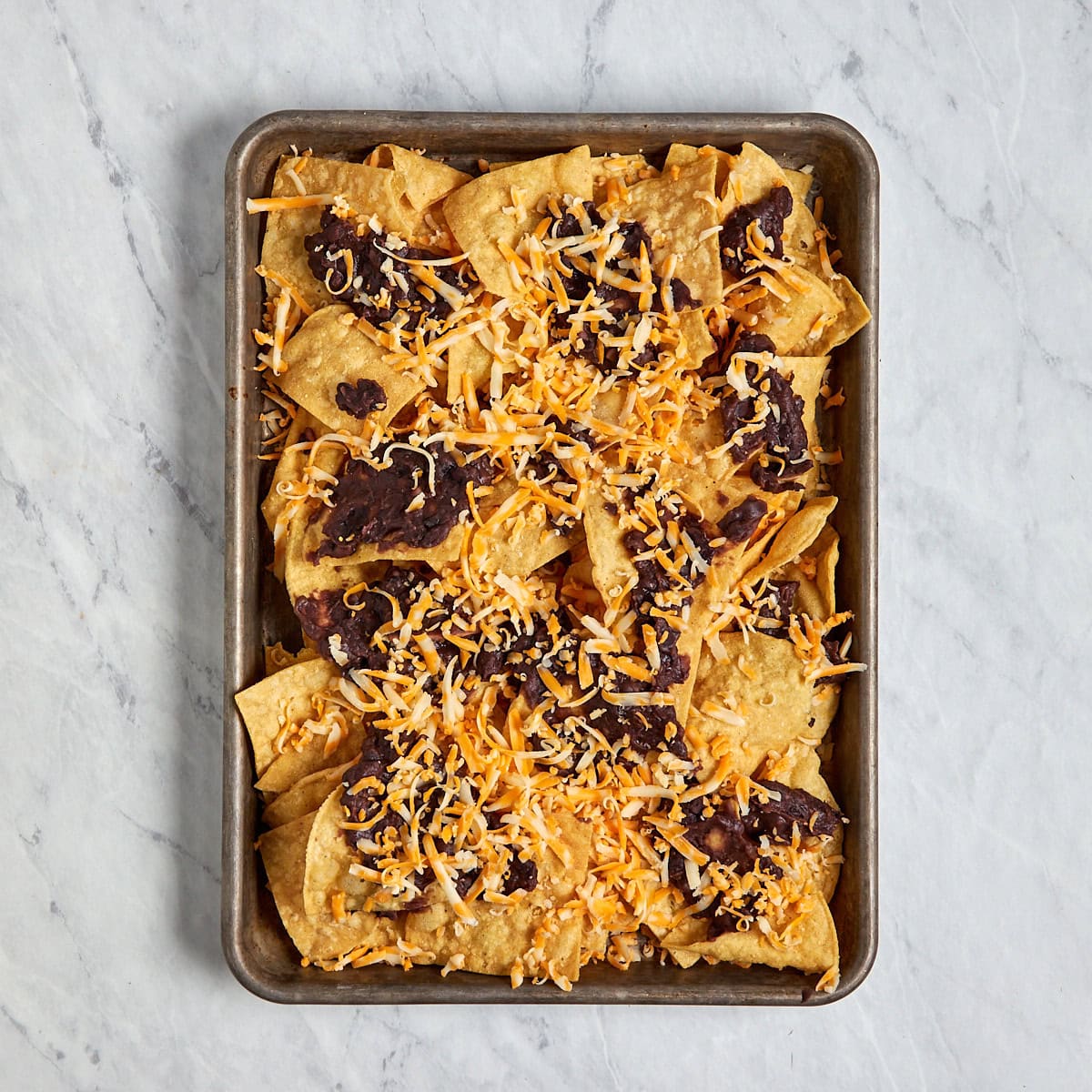 tortilla chips on a sheet pan topped with refried beans and shredded cheese.