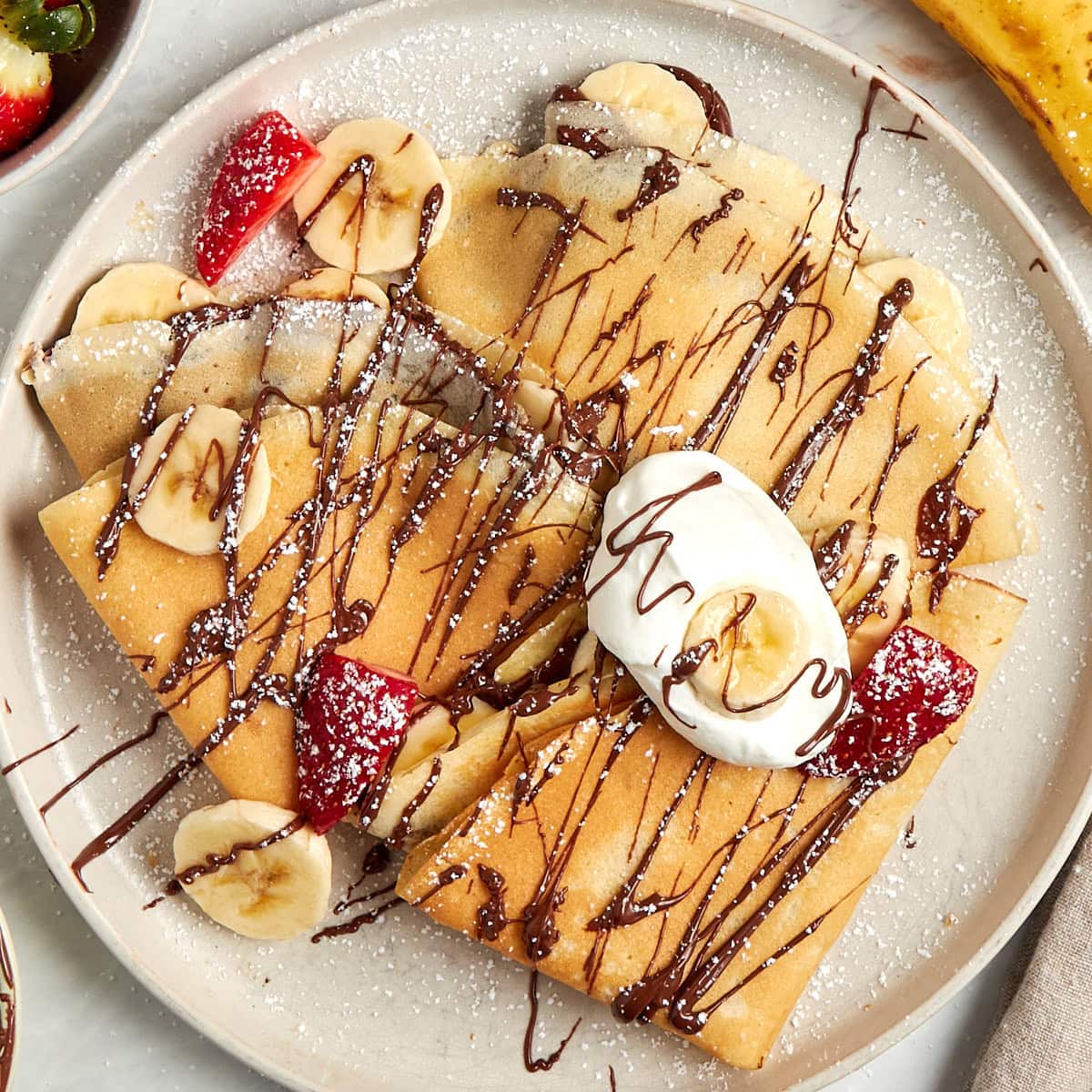 crepes filled with bananas and nutella then drizzled with nutella served on a white plate.
