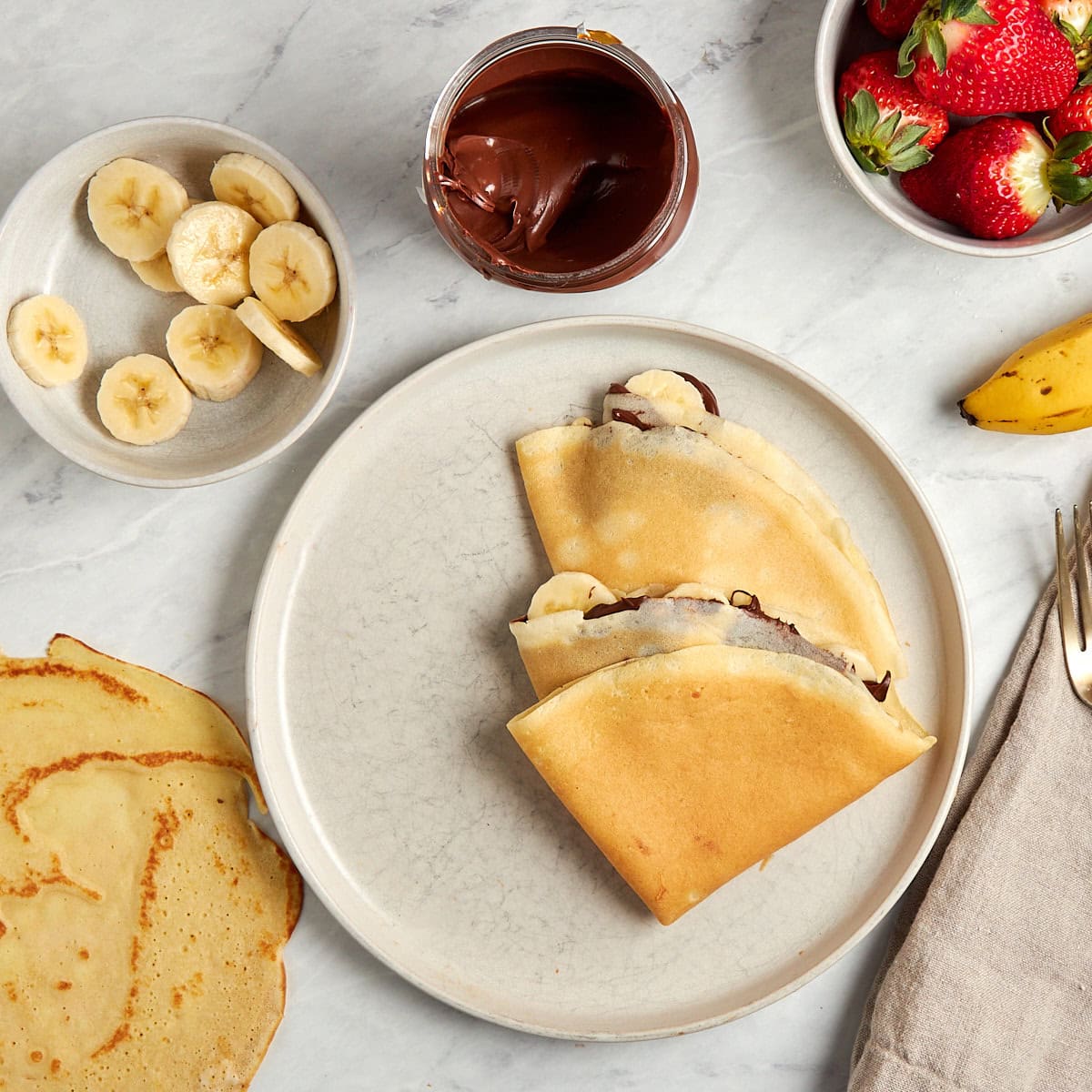 two crepes filled with nutella and bananas folded into quarters and served on a white plate.