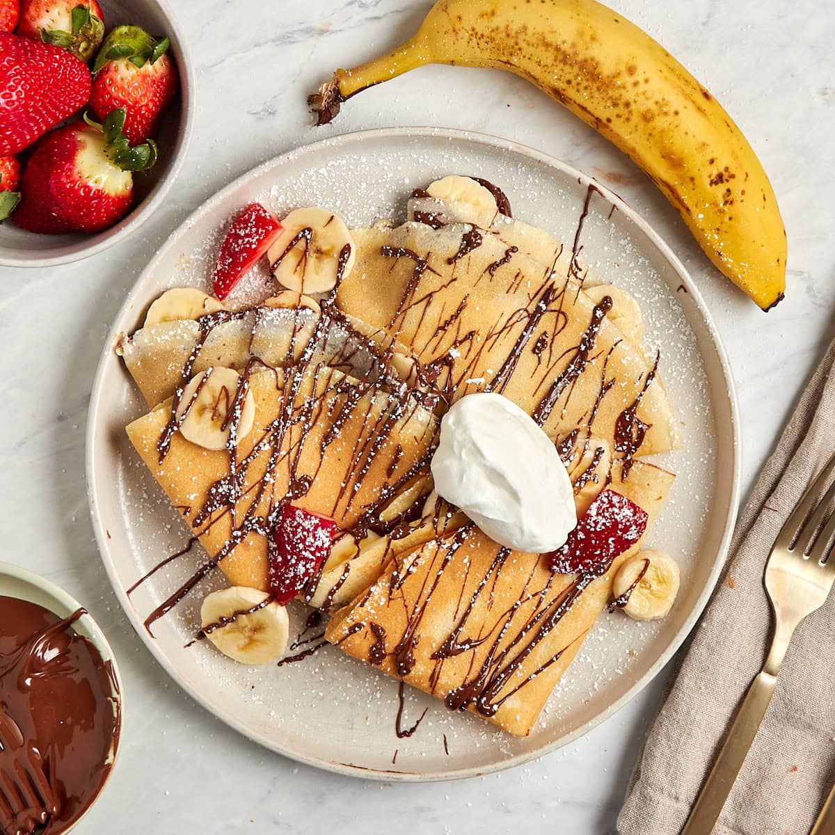 crepes filled with bananas and nutella then drizzled with nutella served on a white plate.