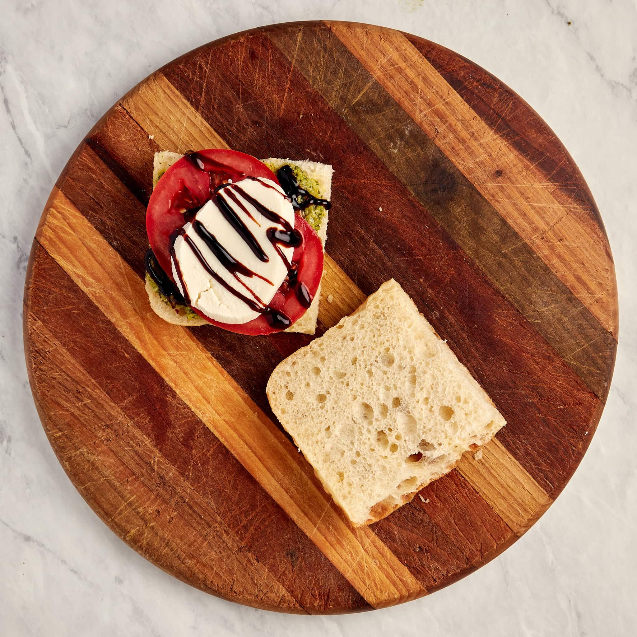 sliced bread with basil pesto, tomato slices, mozzarella, and balsamic glaze on one side.
