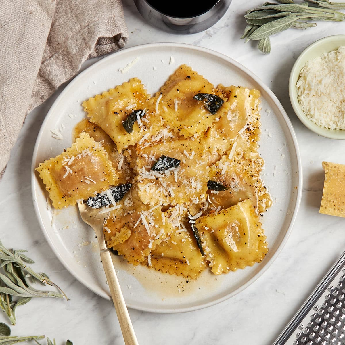 ravioli and sage brown butter topped with shredded cheese on a white plate.