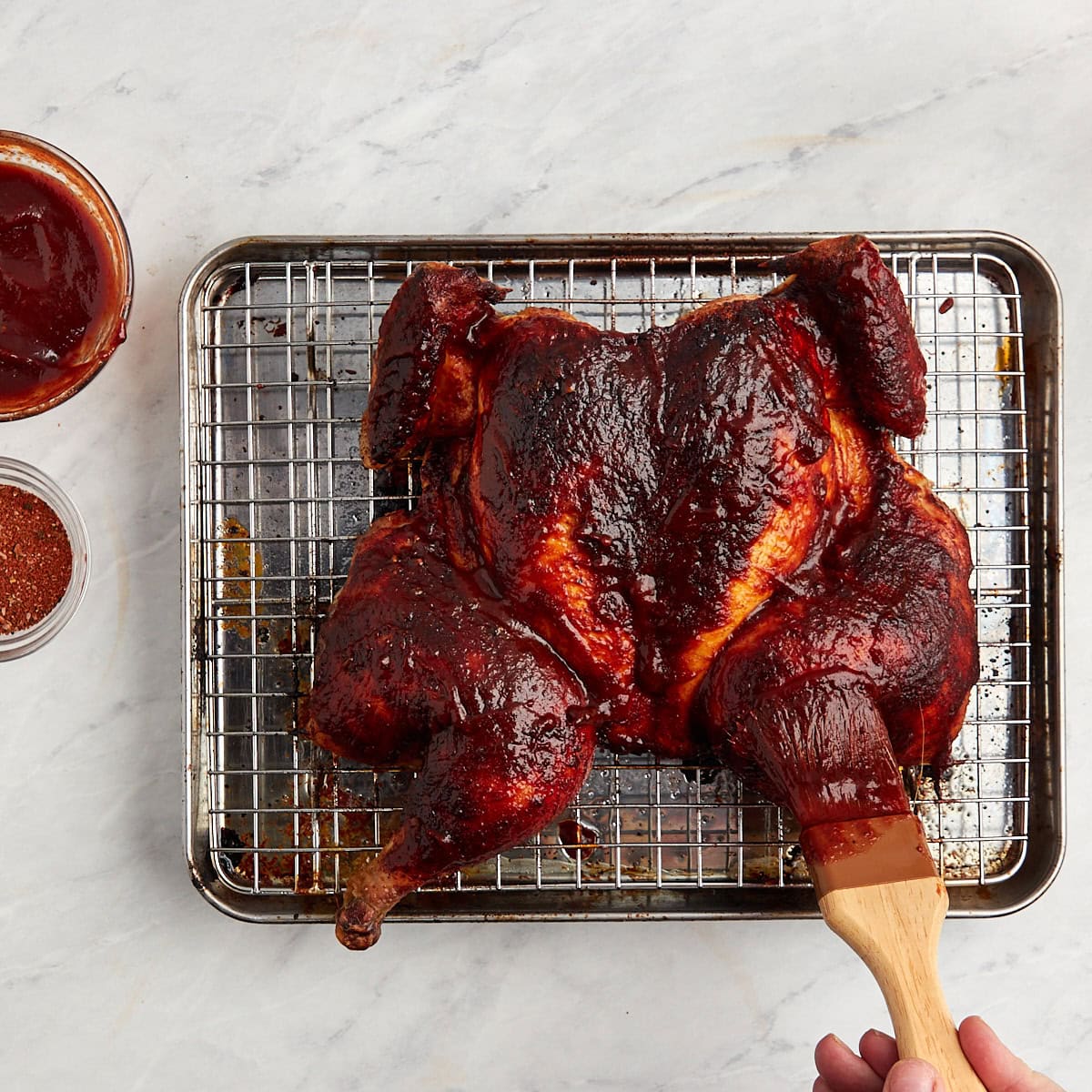 bbq being added to a spatchcock chicken after it has been cooked in the oven.