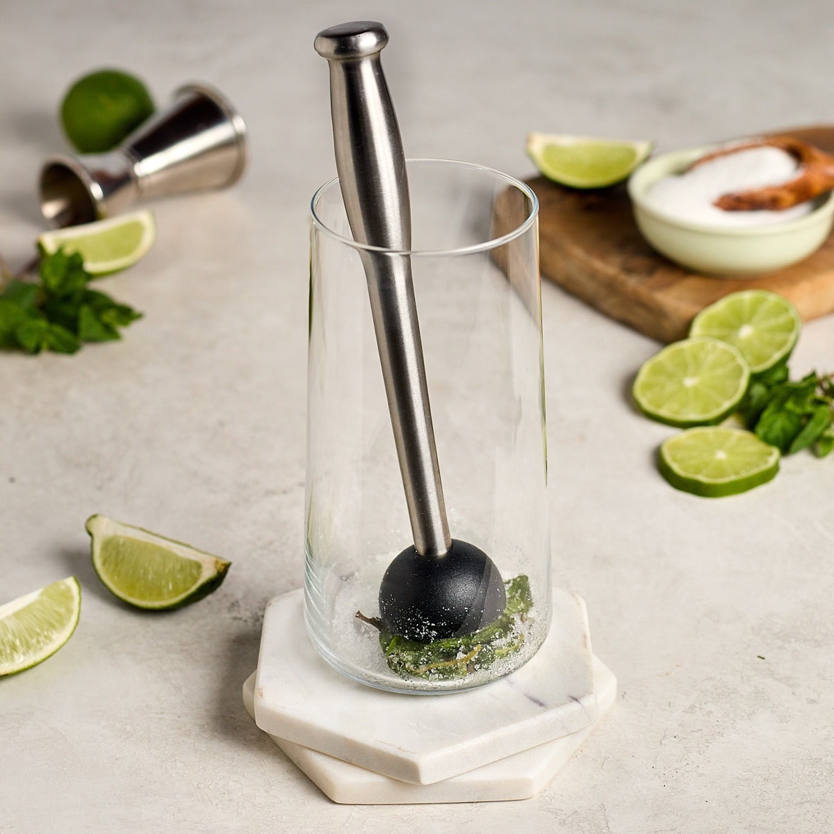 mint being muddled in sugar in a tall glass.