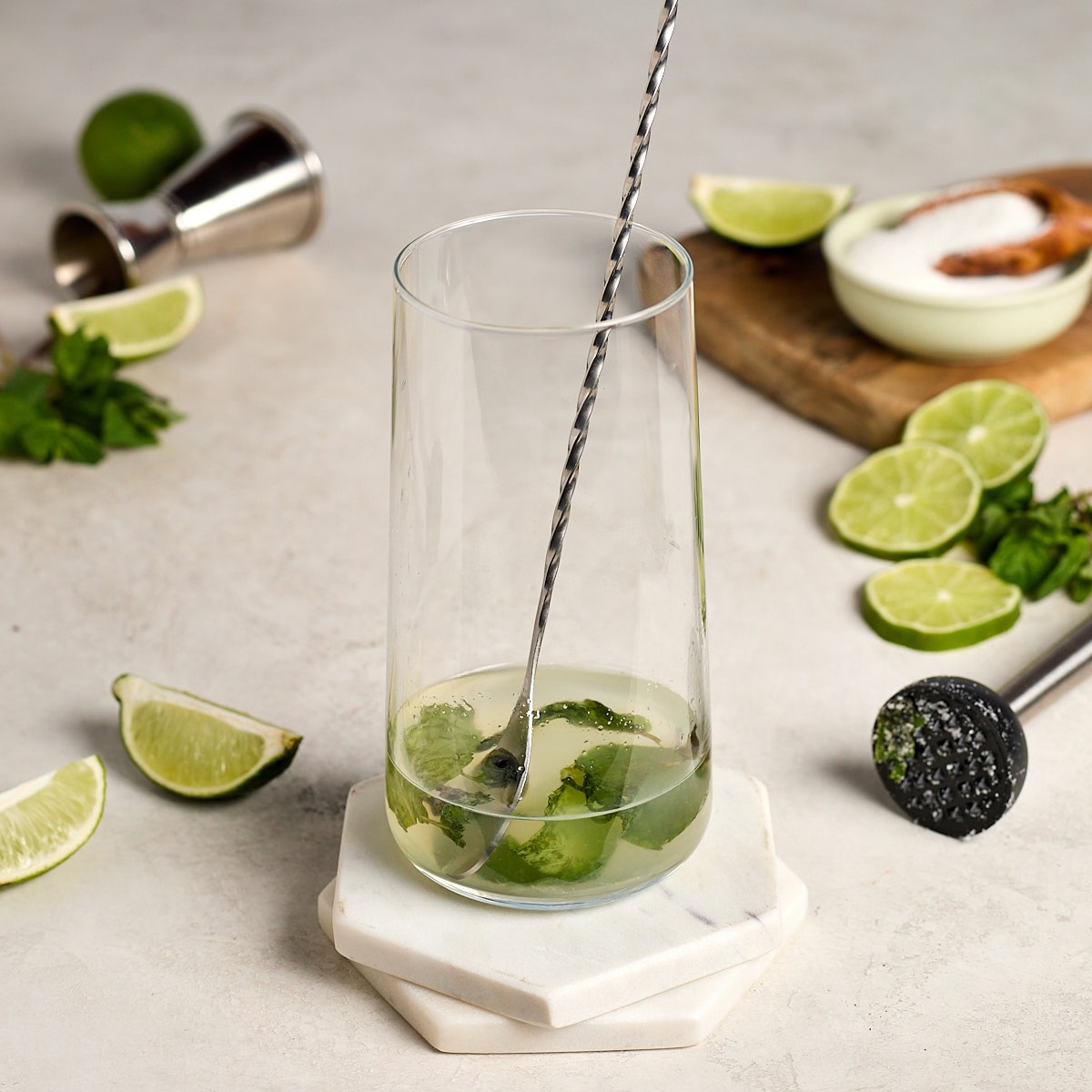 lime juice and rum being stirred into a glass with muddled mint and sugar.