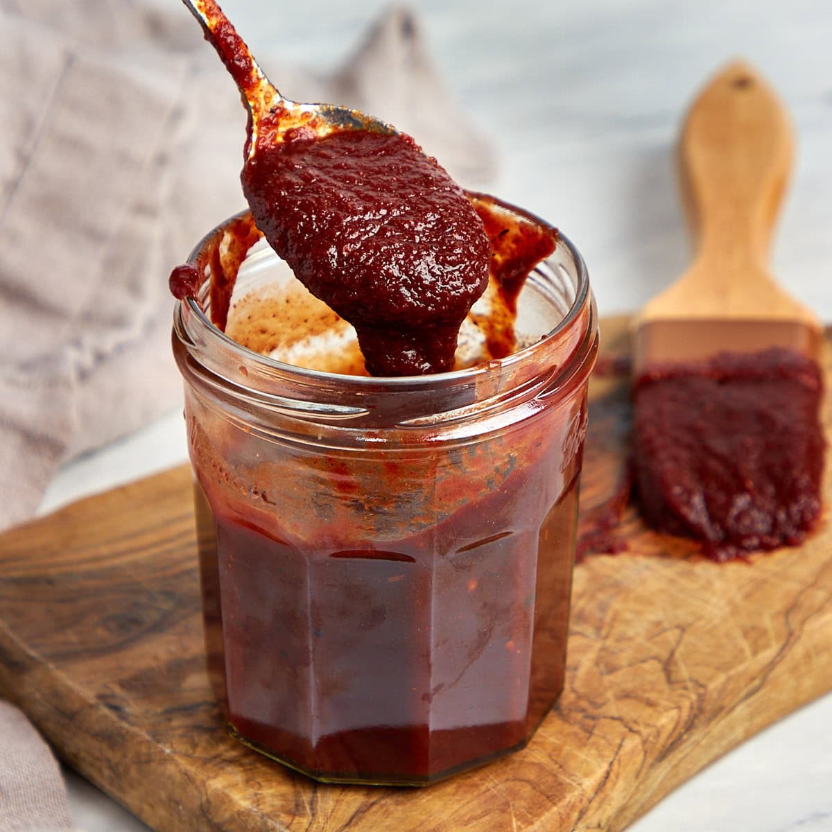 Homemade BBQ sauce in a jar with a spoonful of sauce being taken from the jar.