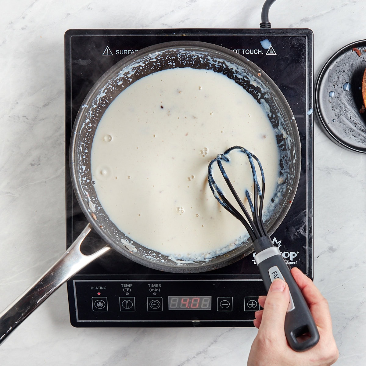 milk being whisked in a skillet with the roux.