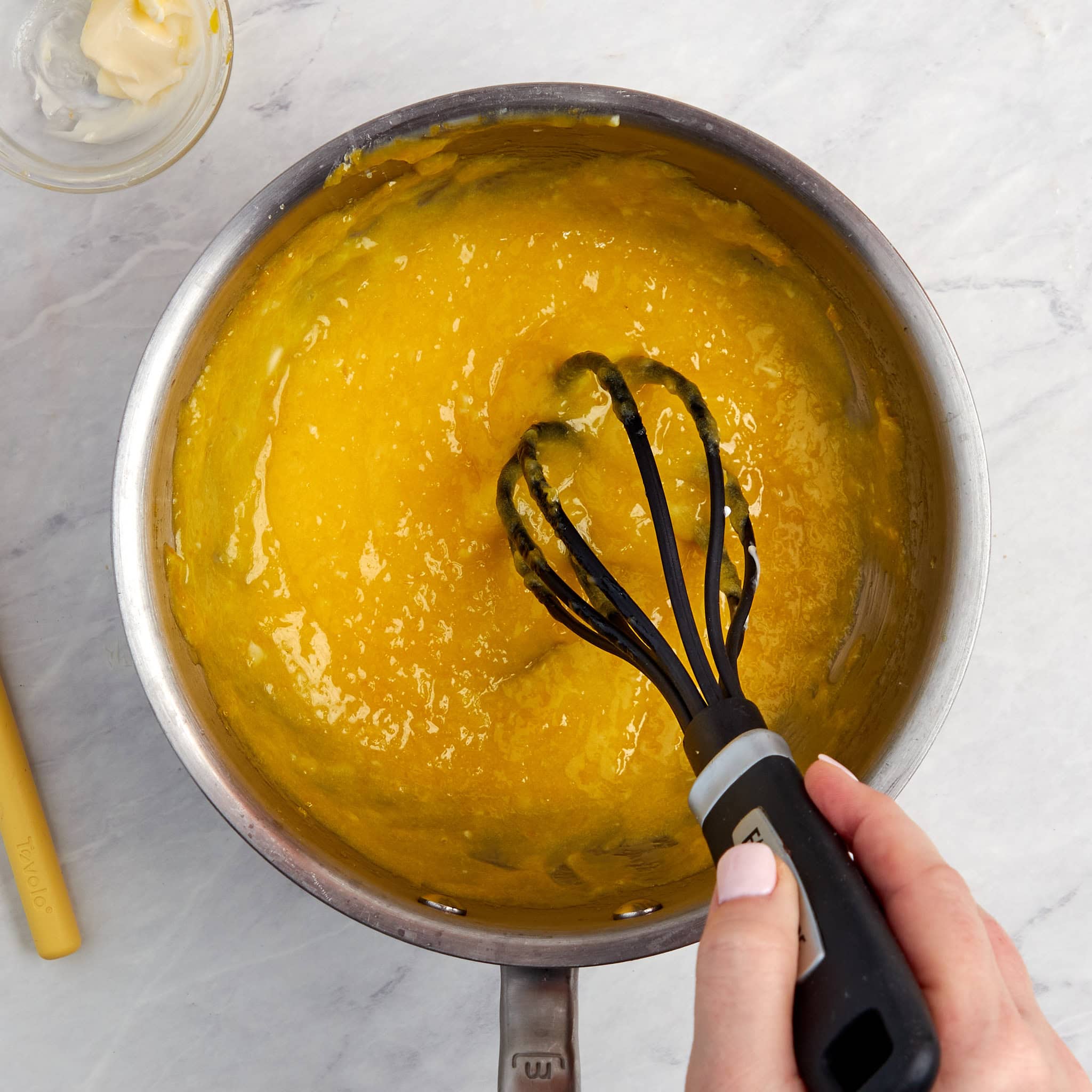 butter being added to the lemon curd in a saucepan.