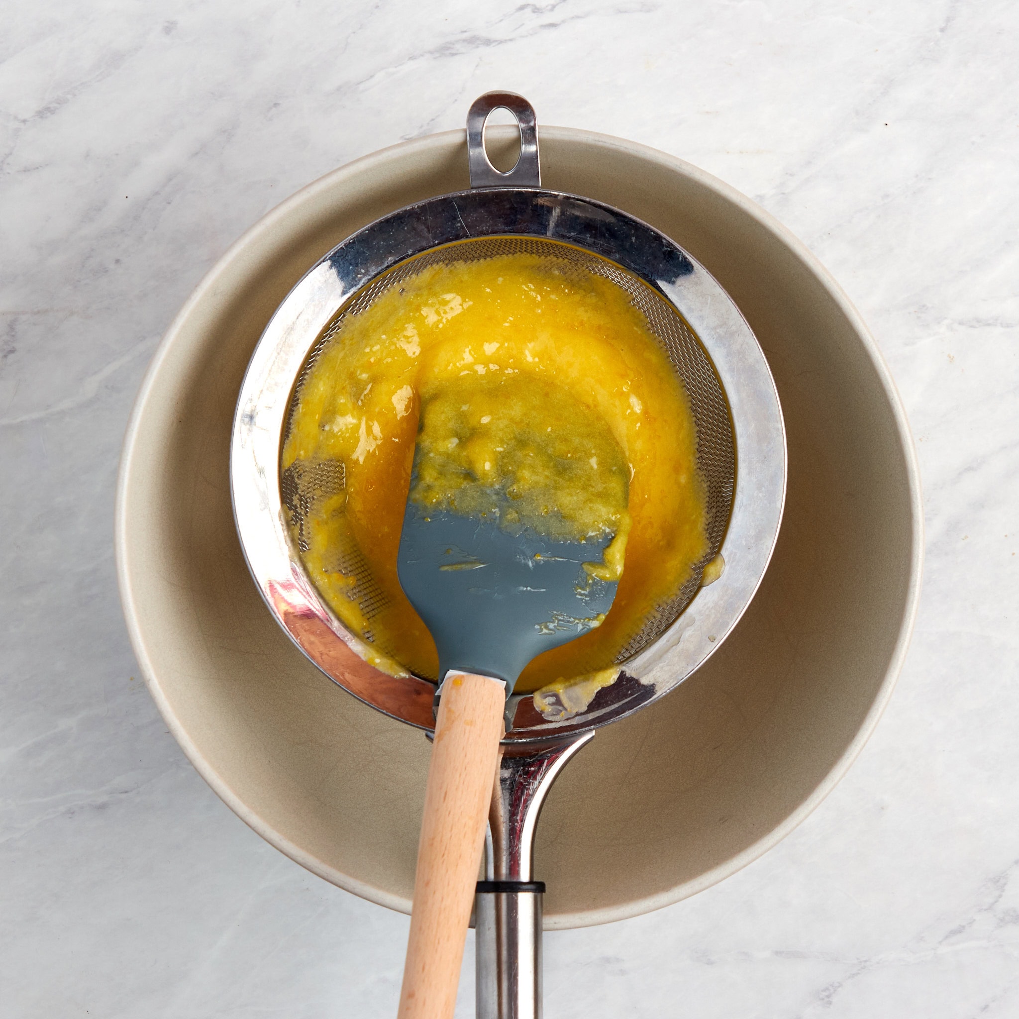 lemon curd being strained into a bowl.