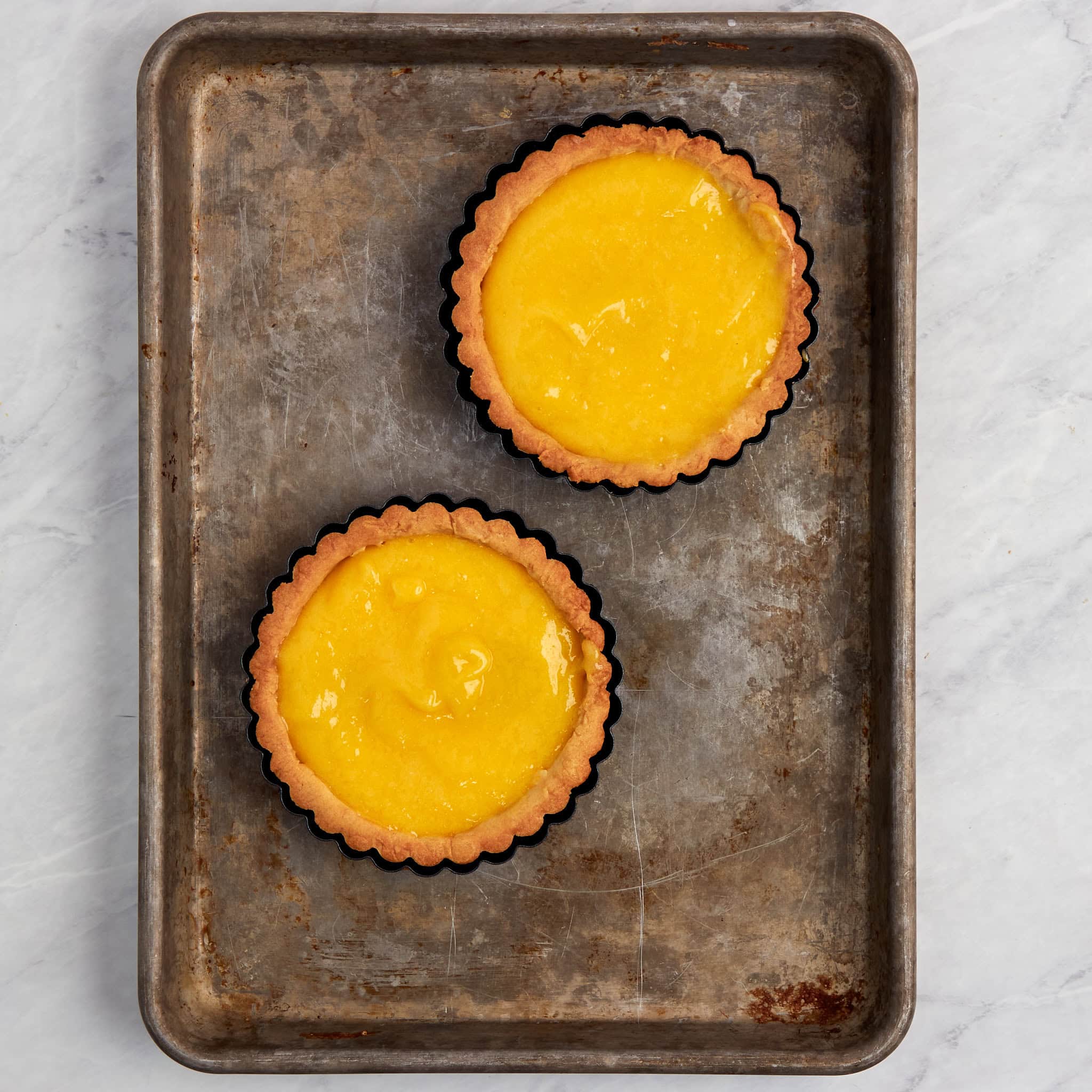 two lemon tarts without any garnishes on a cookie sheet.