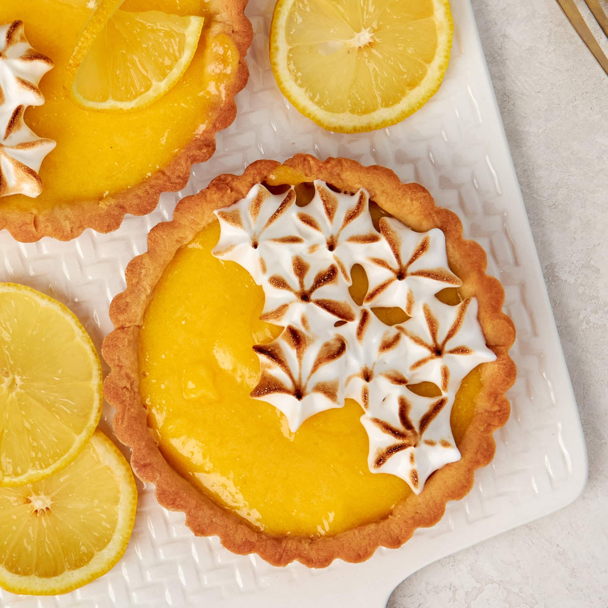 a lemon meringue tart garnished with meringue on a white board.