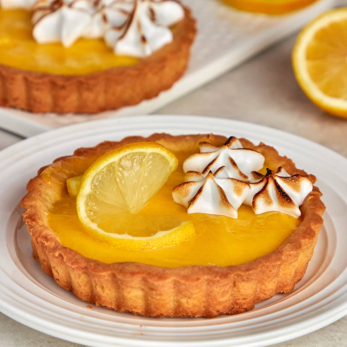 a lemon meringue tart garnished with lemon and meringue on a white plate.