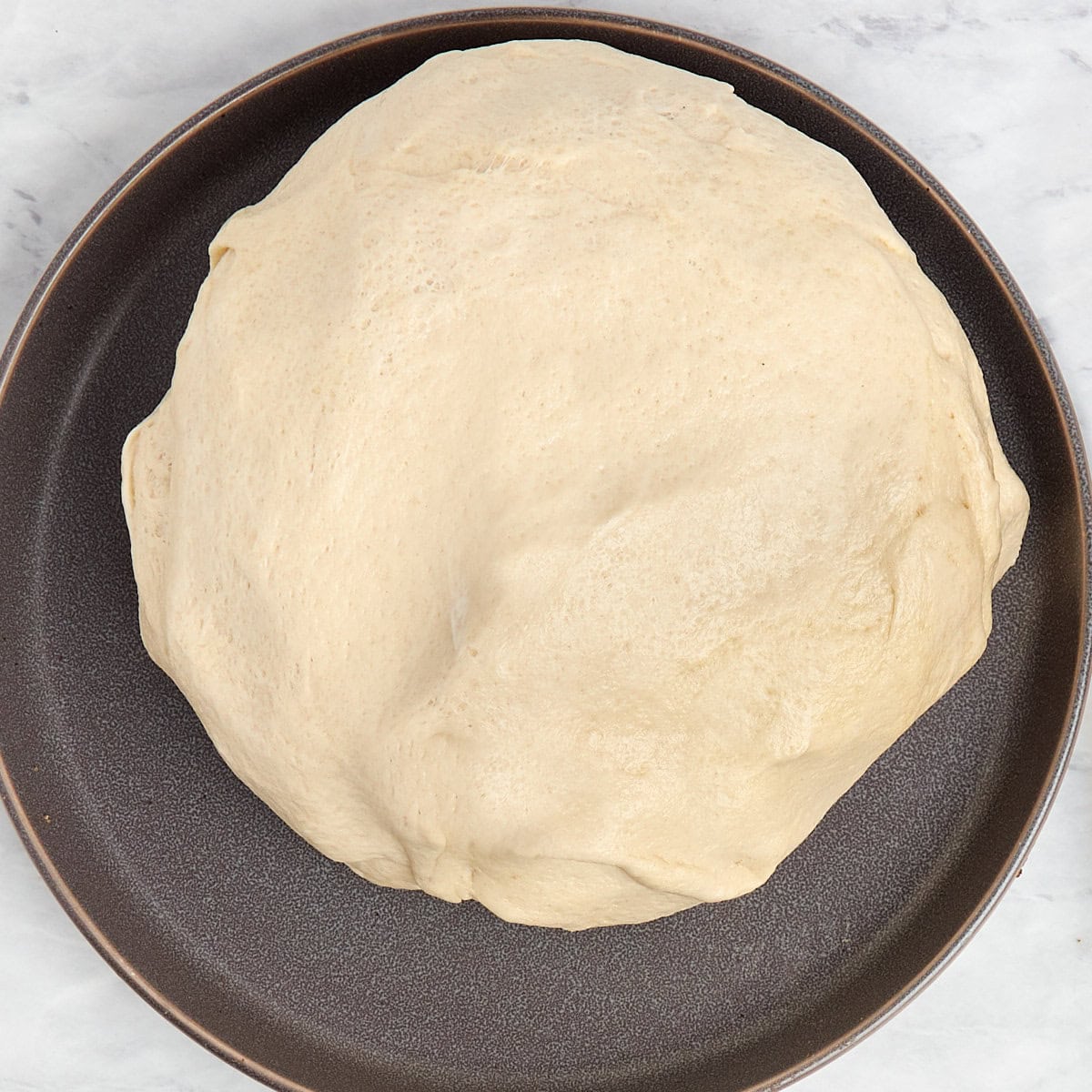 prepared pizza dough on a grey plate.