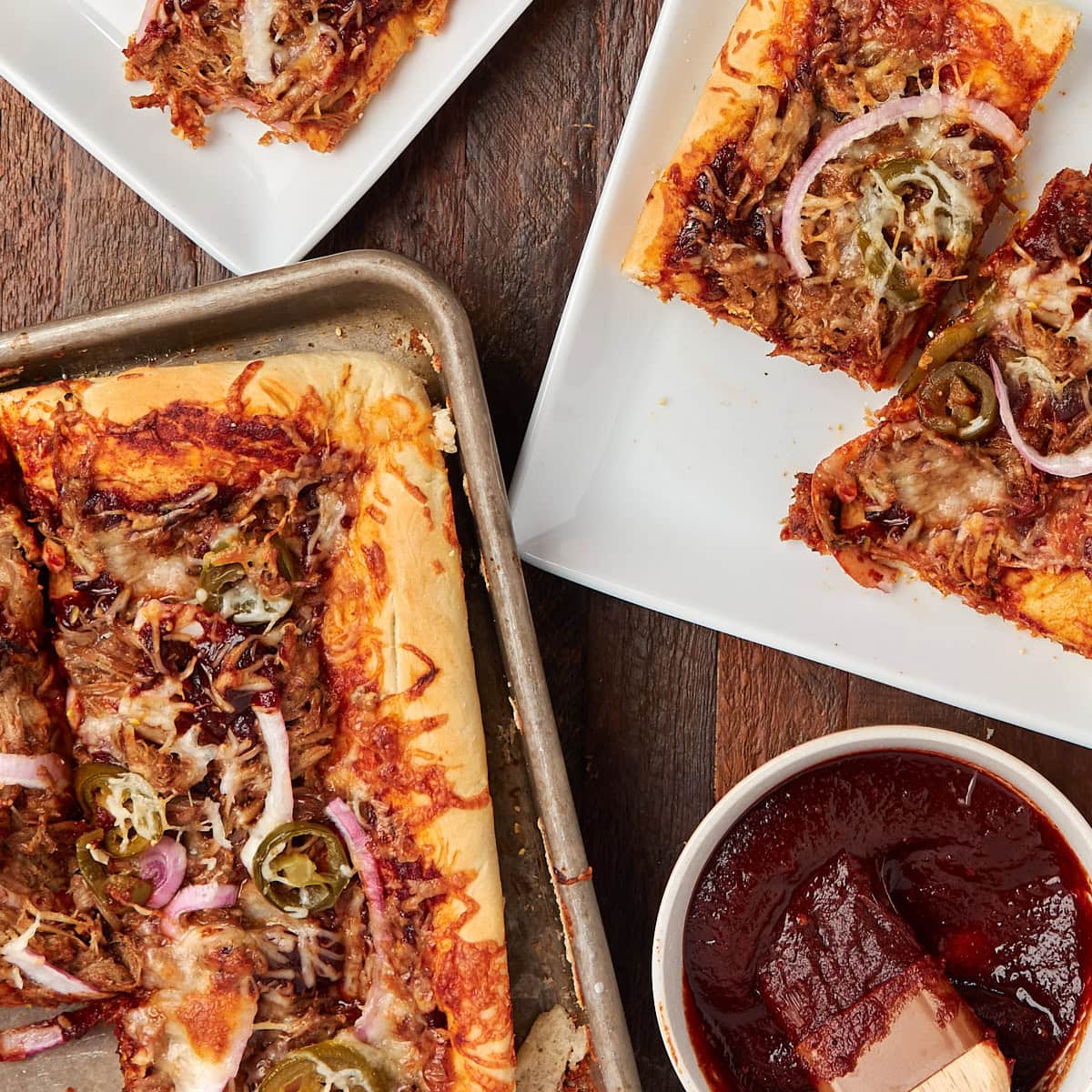pulled pork sheet pan pizza cut into pieces and served on a white plate.