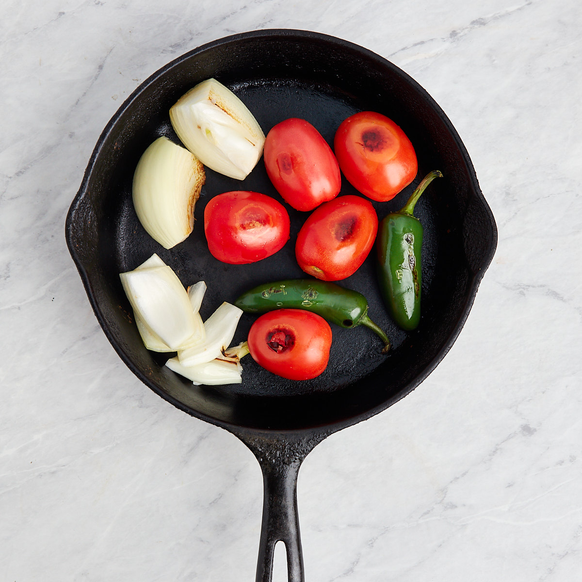 tomatoes, jalapenos, onions being charred in a cast iron pan.
