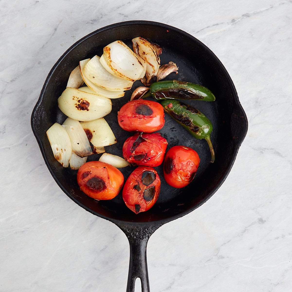 tomatoes, jalapenos, onions being charred in a cast iron pan.