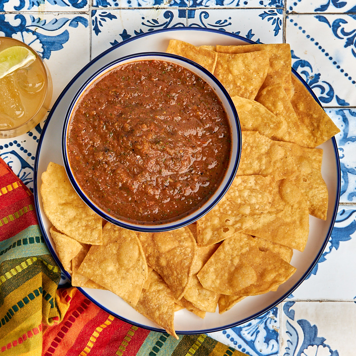 salsa roja in a bowl served on a white plate with tortilla chips.
