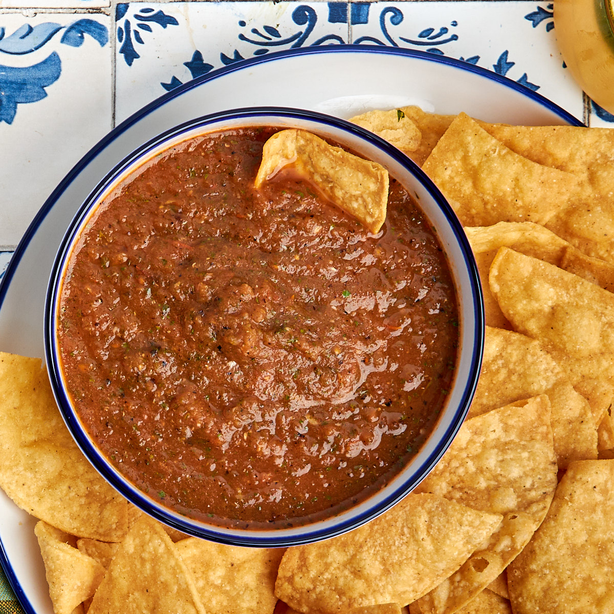 salsa roja in a bowl served on a white plate with tortilla chips.