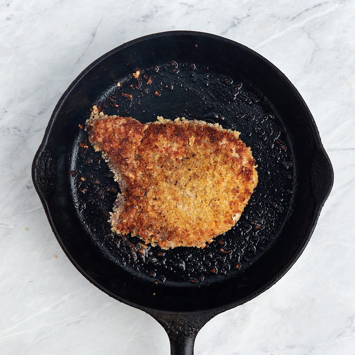 breaded pork chop in a cast iron pan.