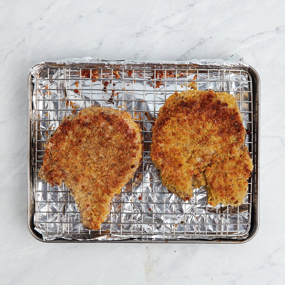 two cooked breaded bone in pork chops on a wire rack.
