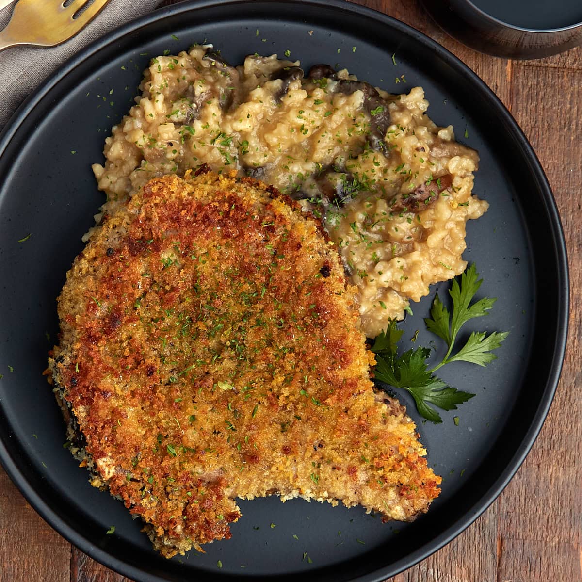 breaded bone in pork chops with mushroom risotto on a black plate.