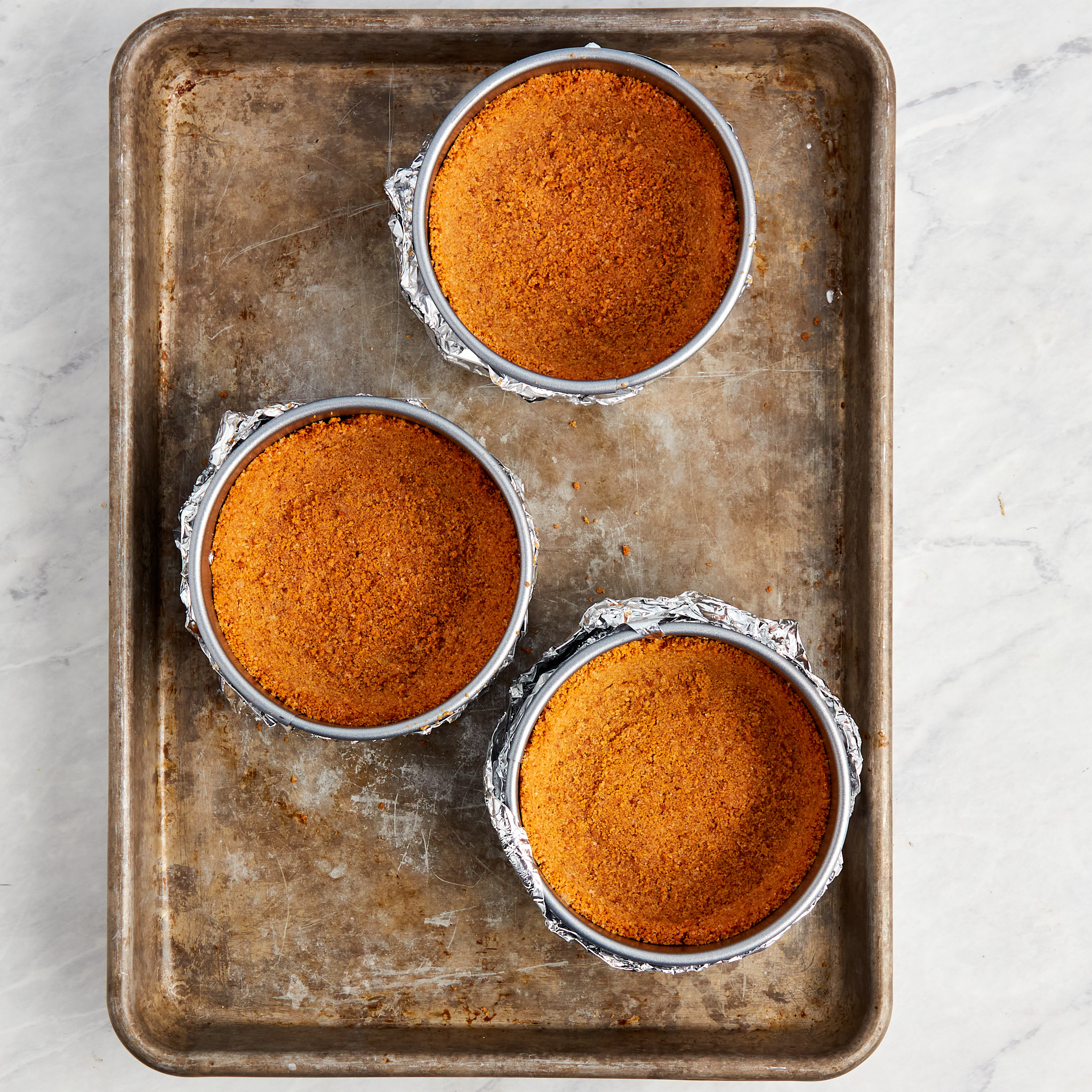 three mini springform pans wrapped in foil with the graham cracker crust added.