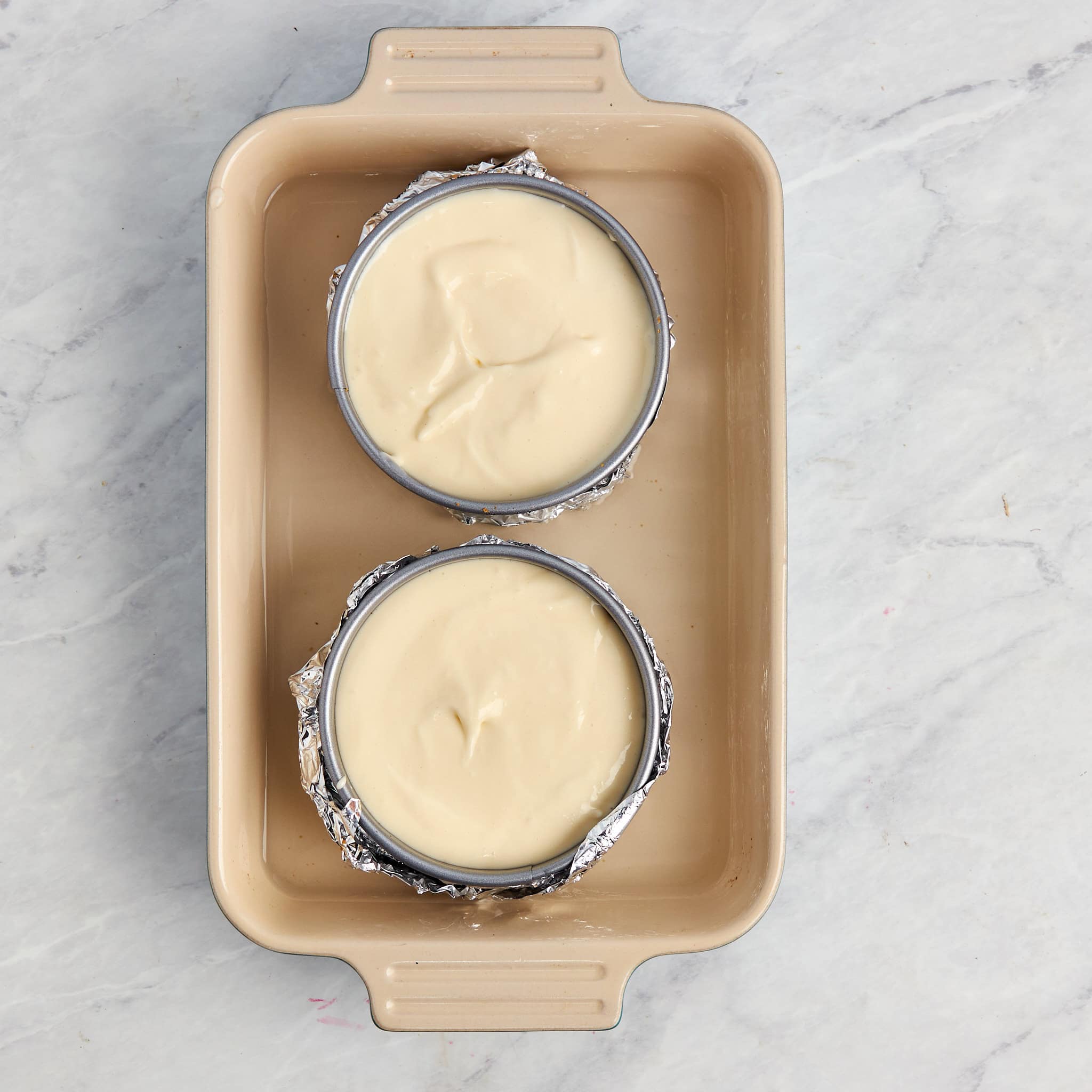 two individual cheesecakes unbaked in a water bath.