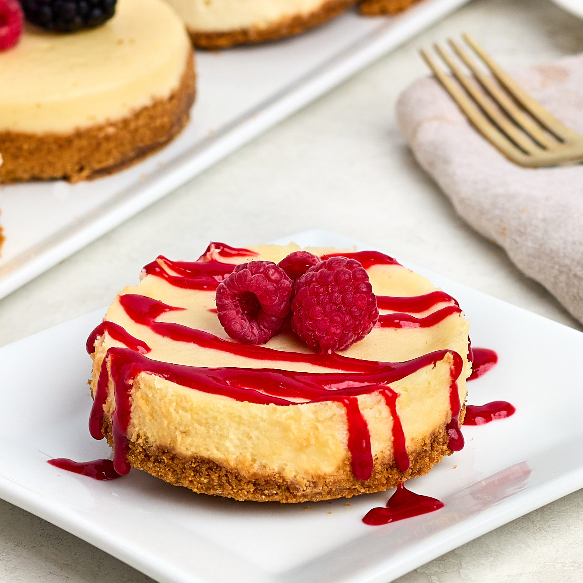 cheesecake topped with raspberry coulis and fresh raspberry served on a white plate.