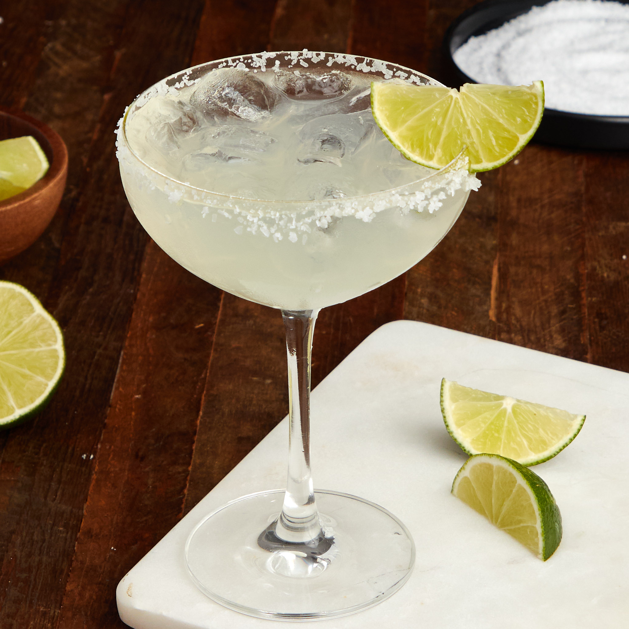 margarita on the rocks with a salted rim in a coupe glass garnished with a wedge of lime.