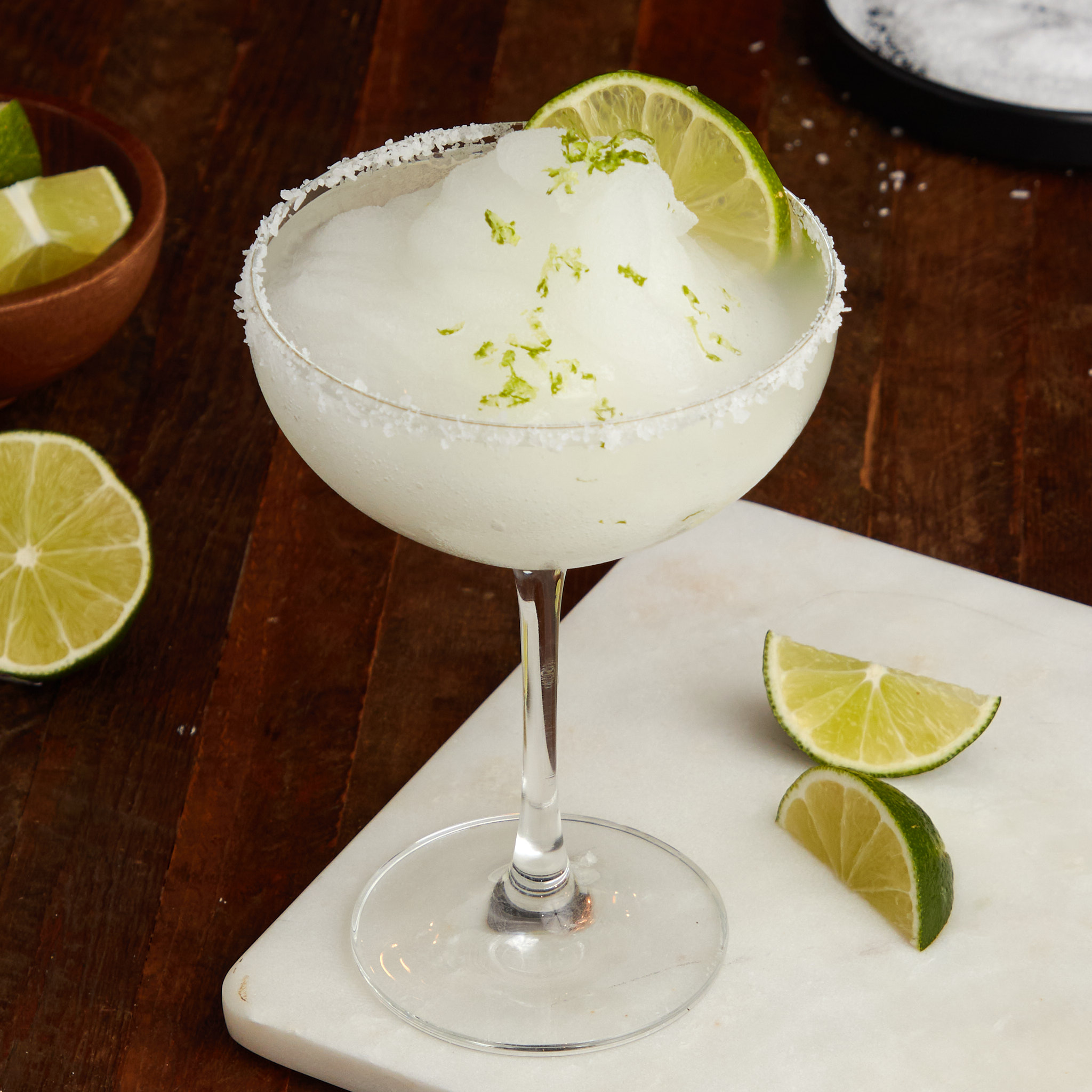 frozen margarita with a salted rim in a coupe glass garnished with a wedge of lime.