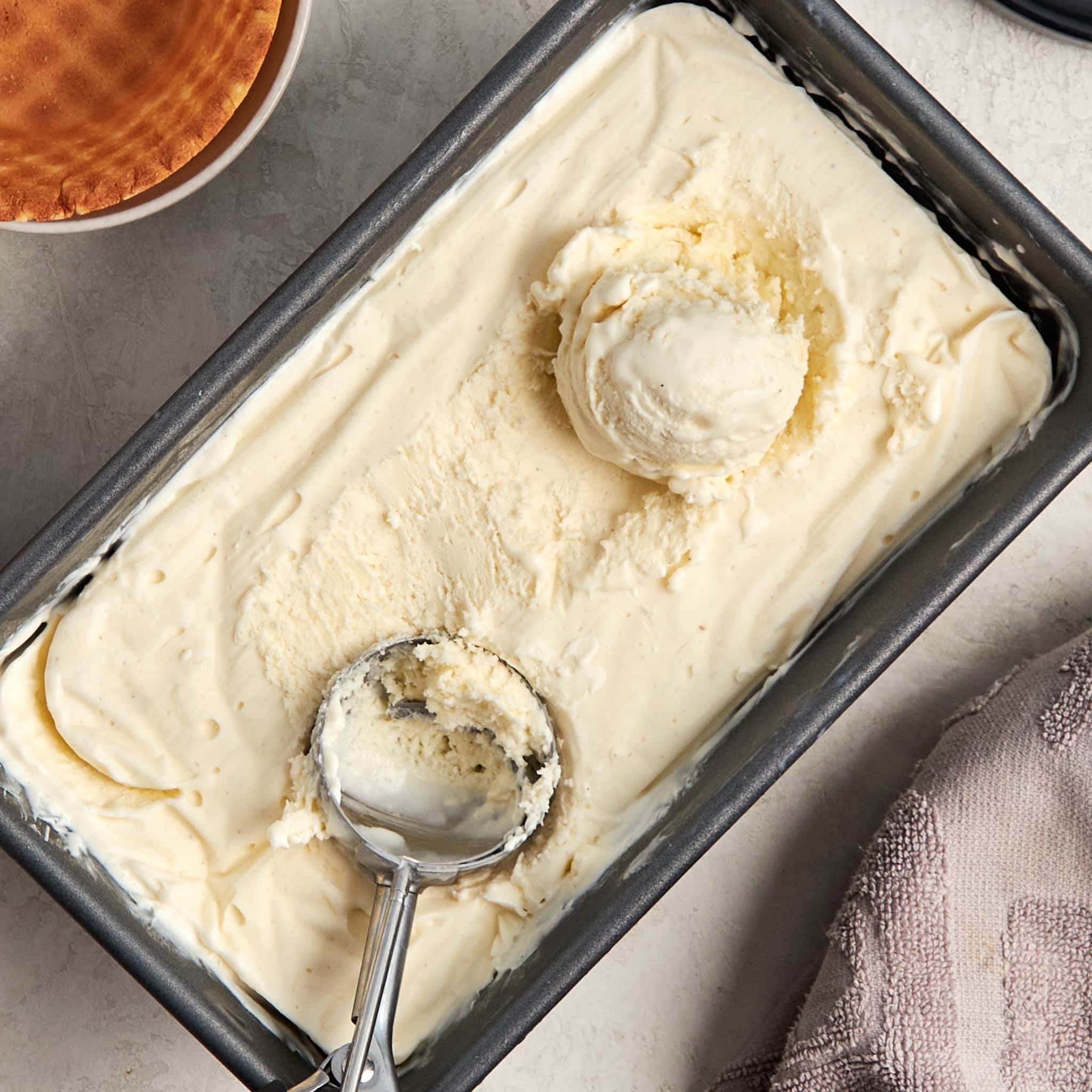 frozen vanilla ice cream in a loaf pan with an ice cream scoop and one scoop of ice cream.