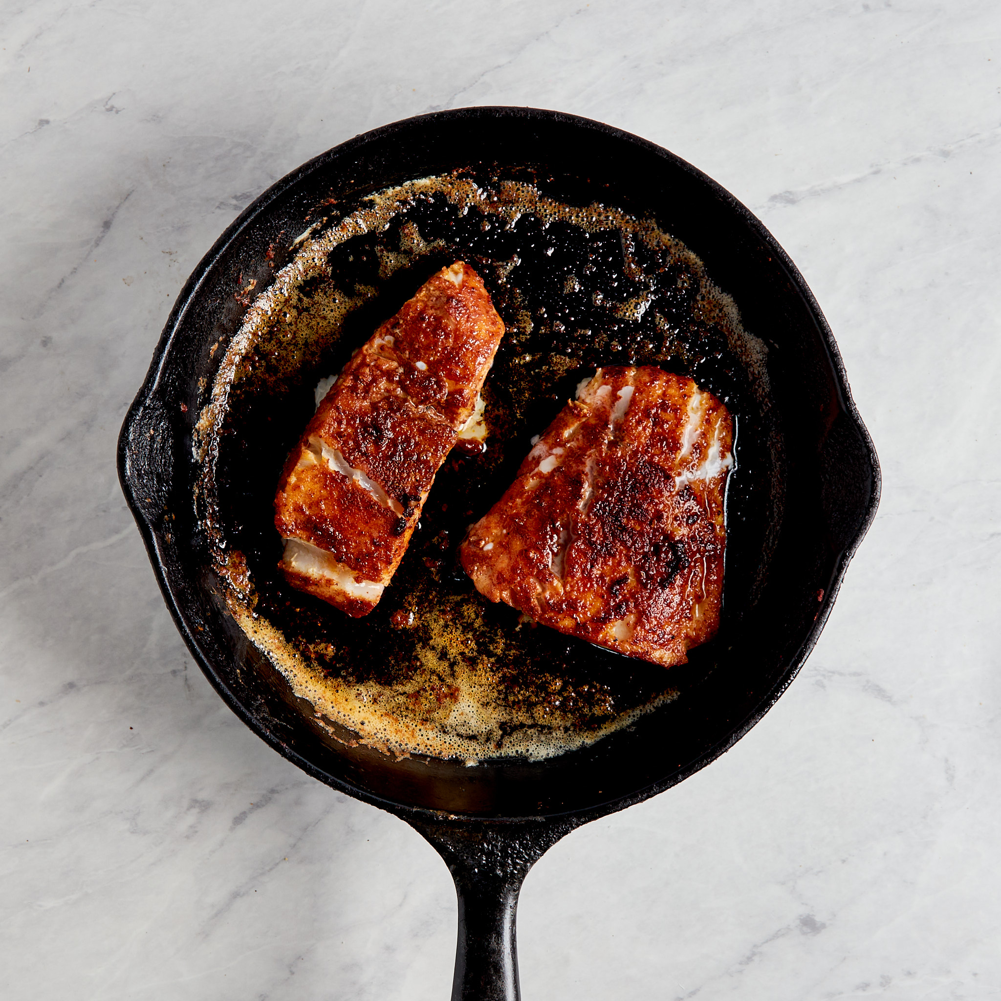 cod being cooked in a cast iron skillet.
