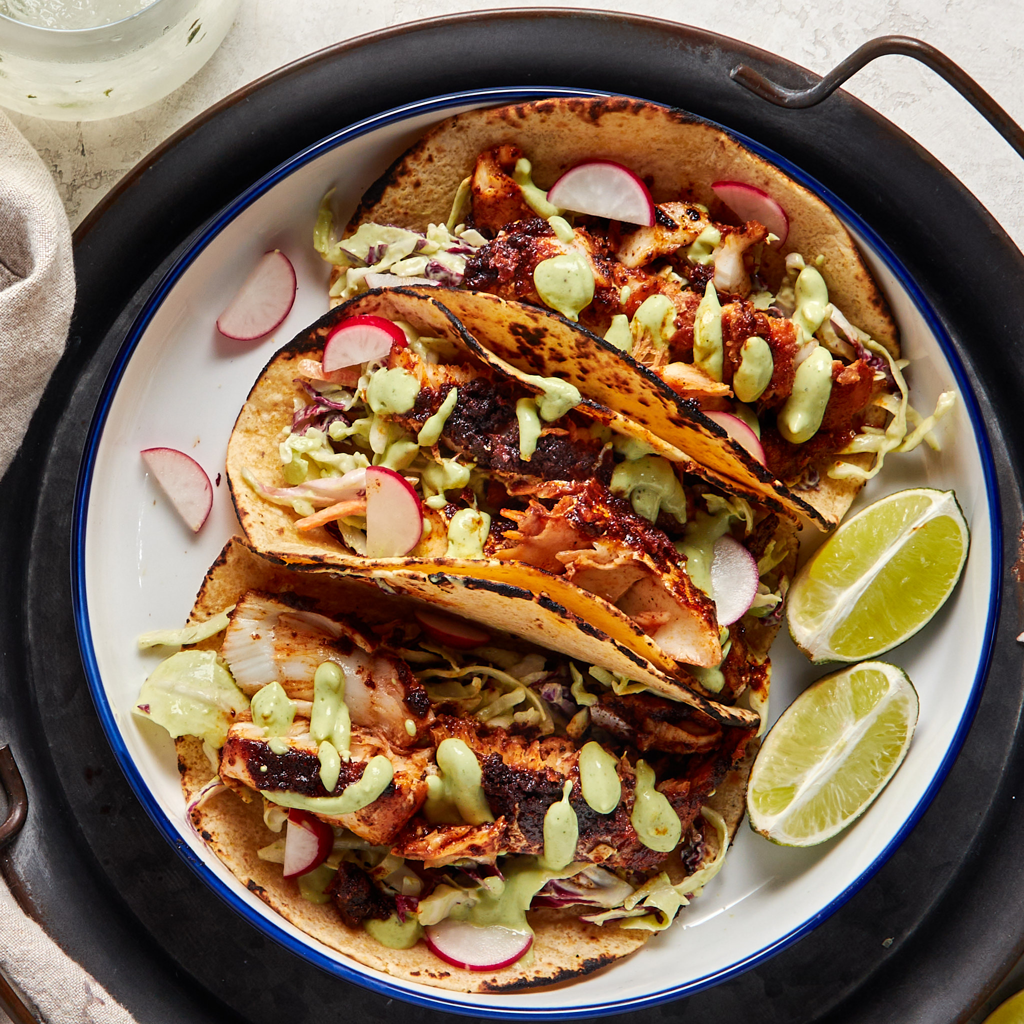 3 blackened fish tacos topped with cilantro lime dressing and shredded cabbage served on a white plate.