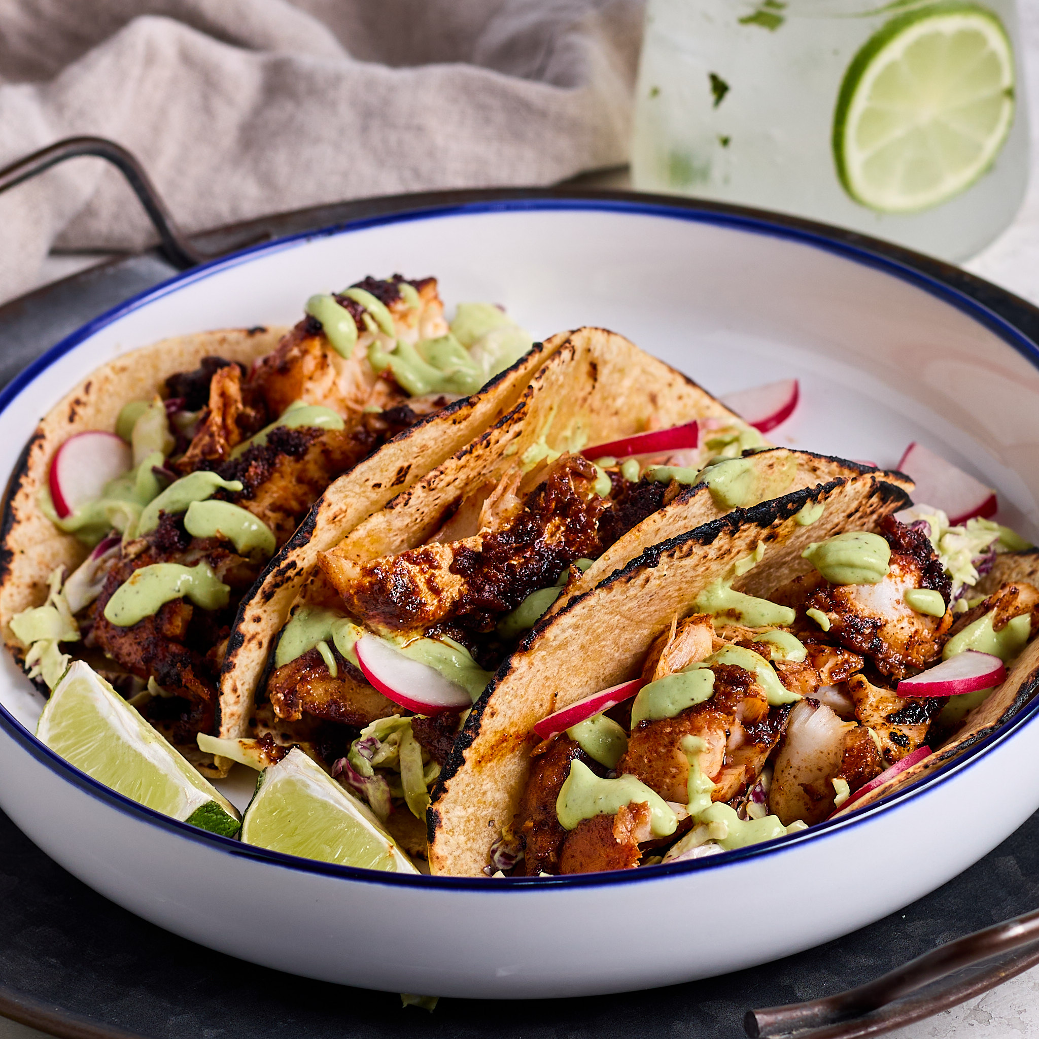 3 blackened fish tacos topped with cilantro lime dressing and shredded cabbage served on a white plate.