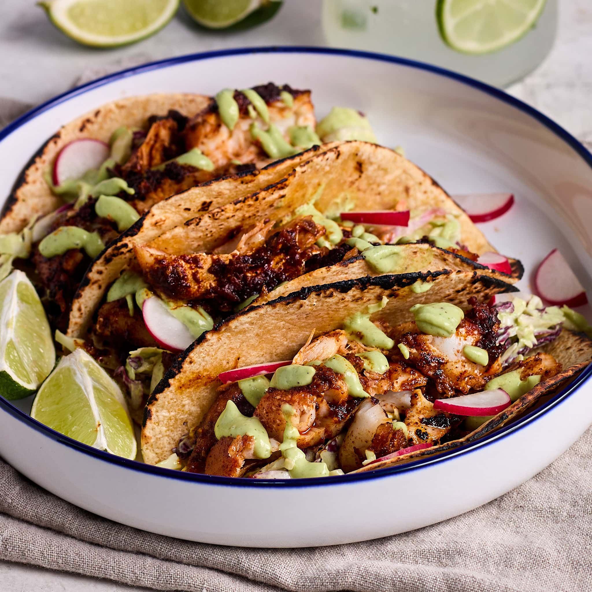 3 blackened fish tacos topped with cilantro lime dressing and shredded cabbage served on a white plate.