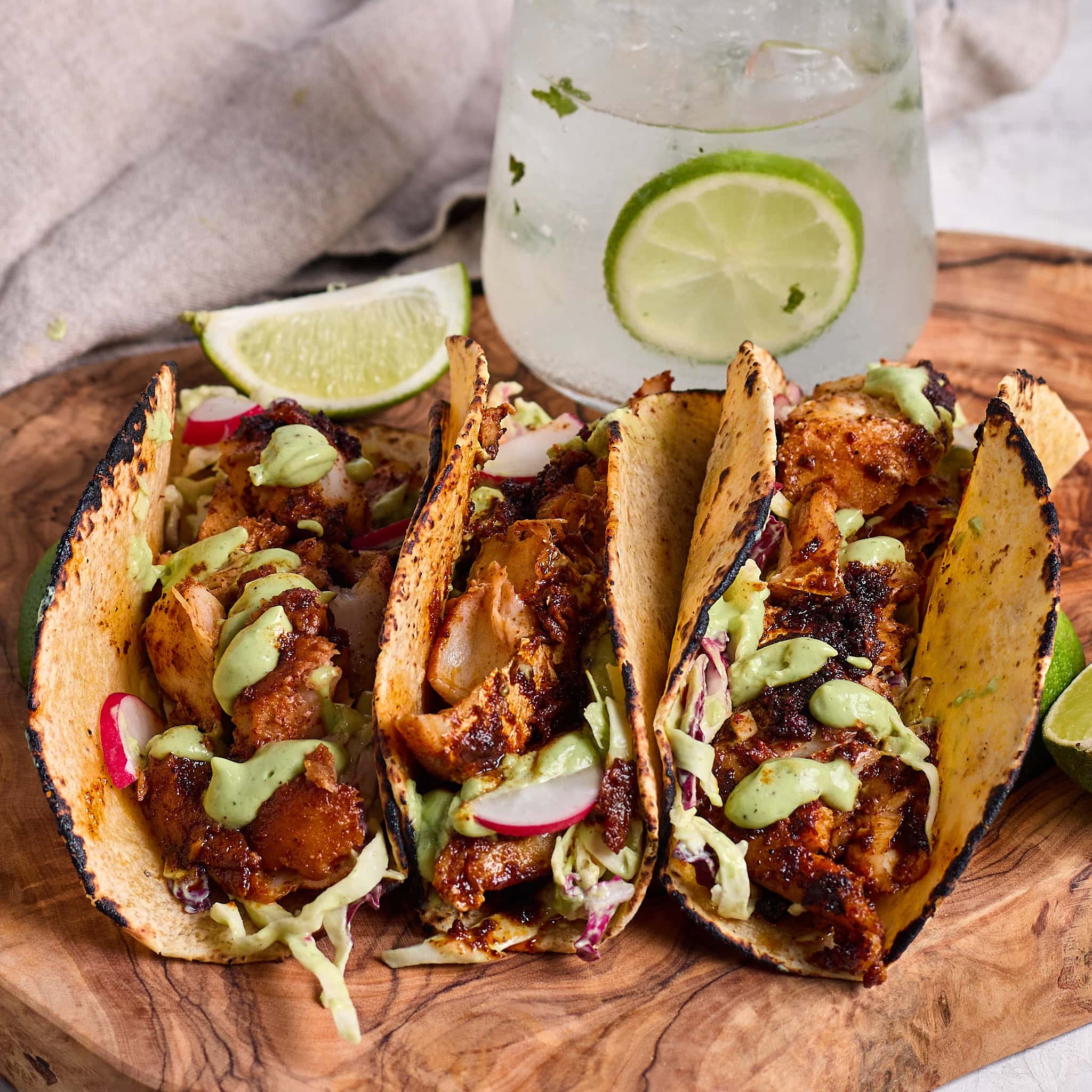 3 blackened fish tacos topped with cilantro lime dressing and shredded cabbage served on a wood board.