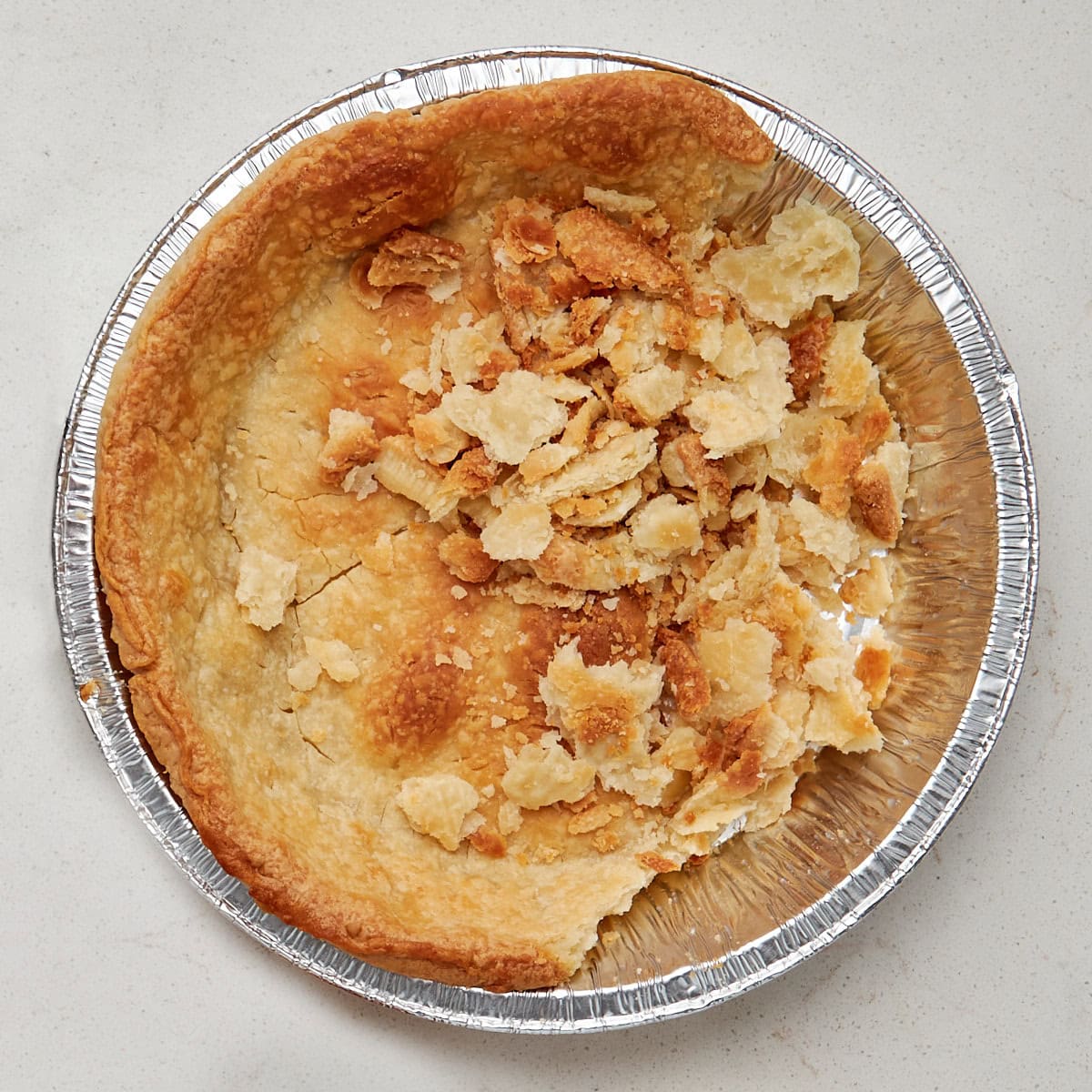 baked pie crust in an aluminum pan that is being broken up into bite size pieces.