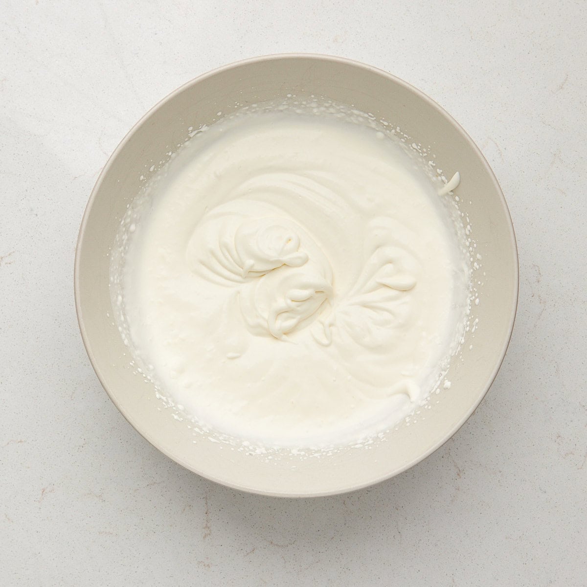 Heavy cream beaten into soft peaks in a white bowl.