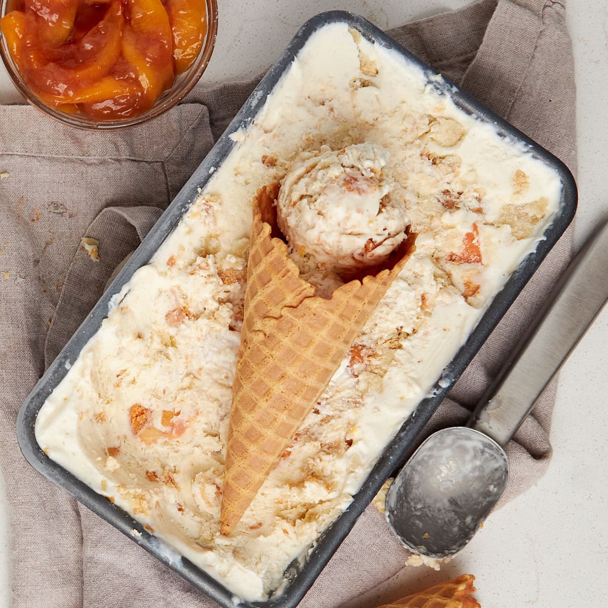 no churn peach ice cream with a waffle cone and scoops of ice cream laying on top.
