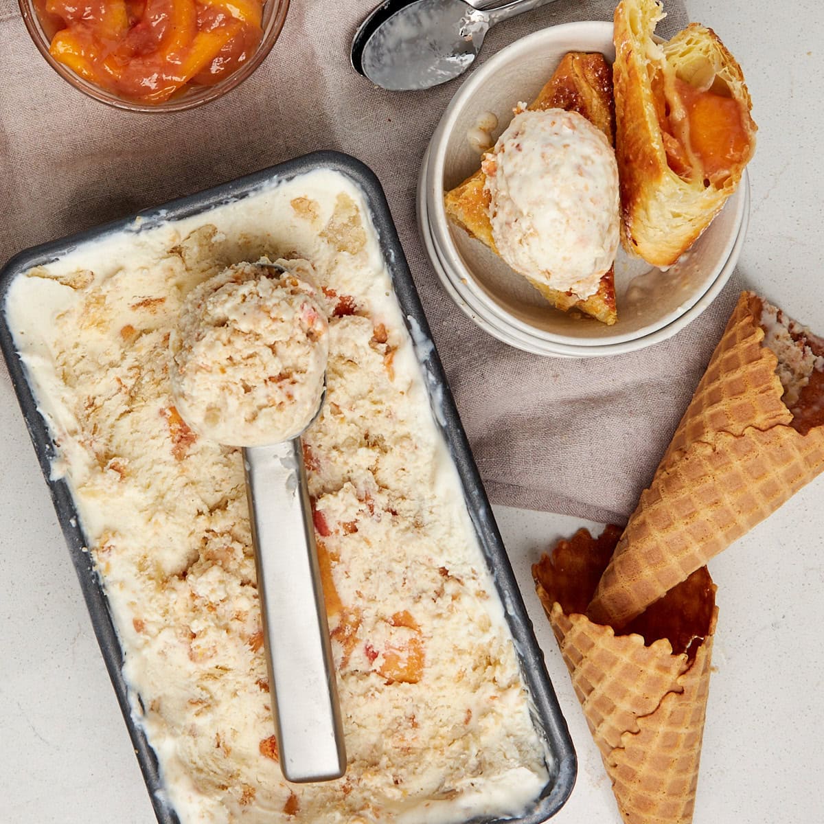 scoop of ice cream laying on top peach ice cream and a peach turnover in a bowl topped with ice cream.