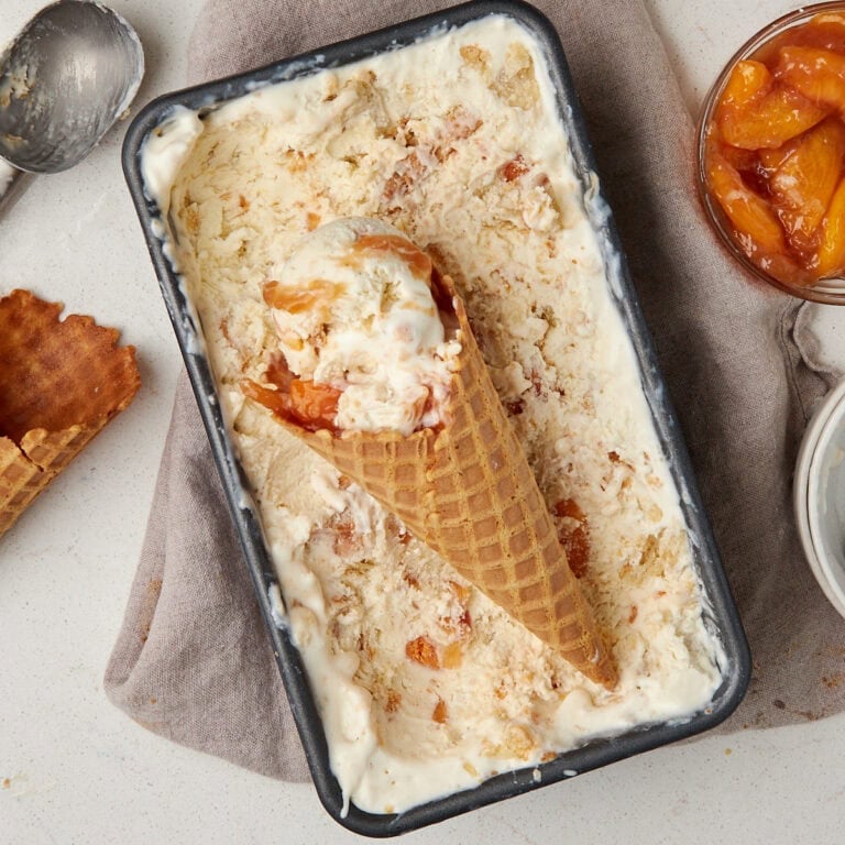 no churn peach ice cream with a waffle cone and scoops of ice cream laying on top.