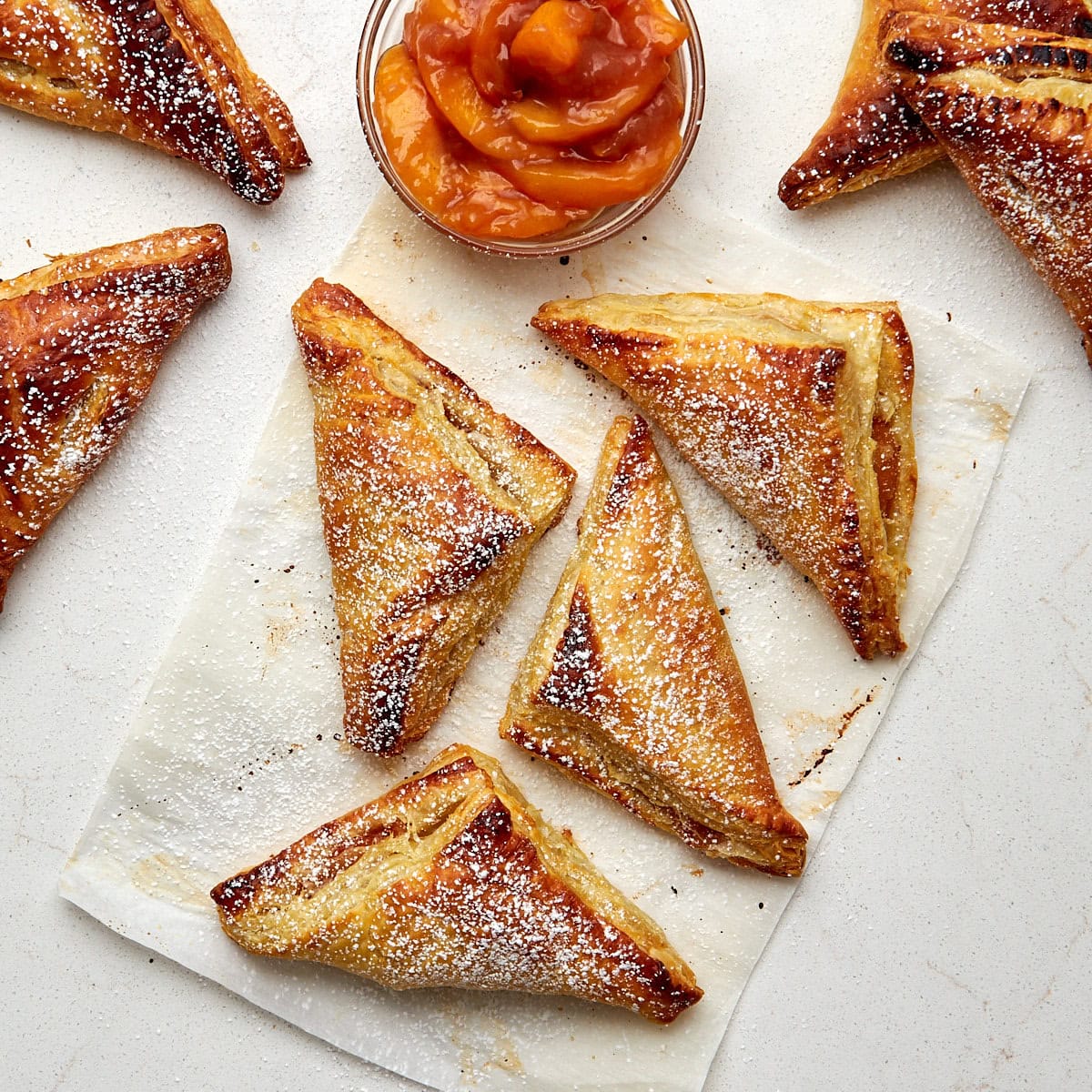 8 baked turnovers on parchment dusted with powdered sugar.