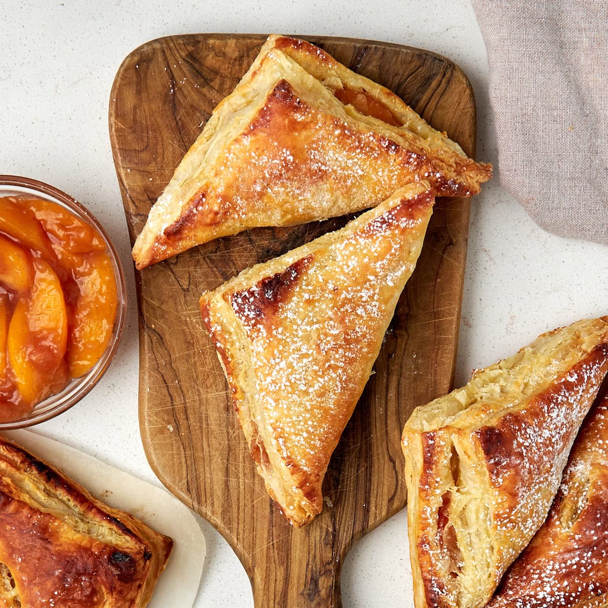 two peach turnovers on a wood cutting board with a side of peach pie filling.