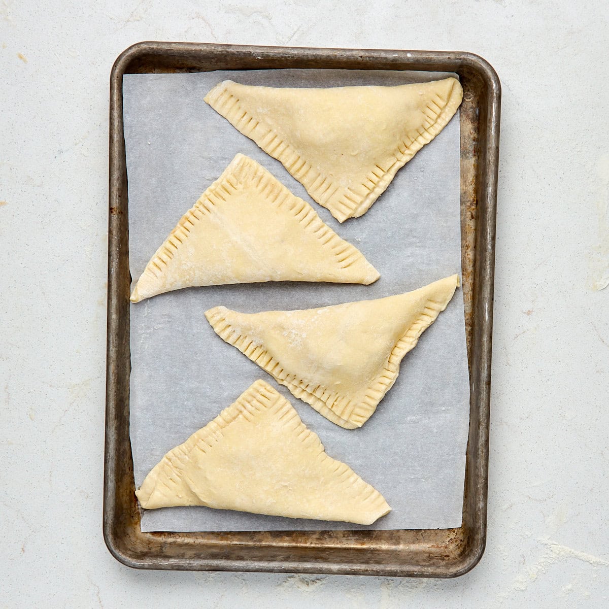4 unbaked turnovers on a sheet pan lined with parchment paper.
