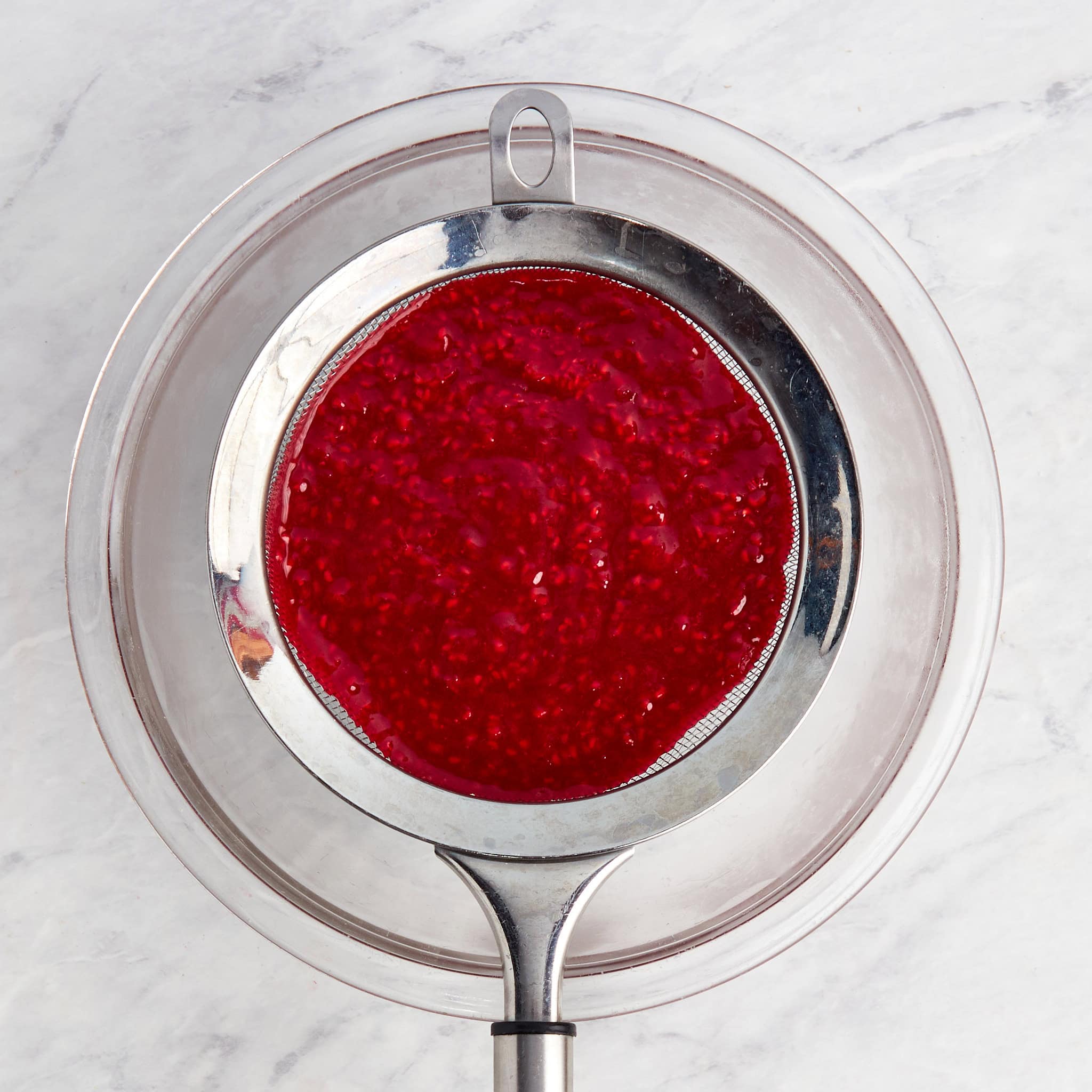 raspberry coulis being strained through a fine mesh strainer.