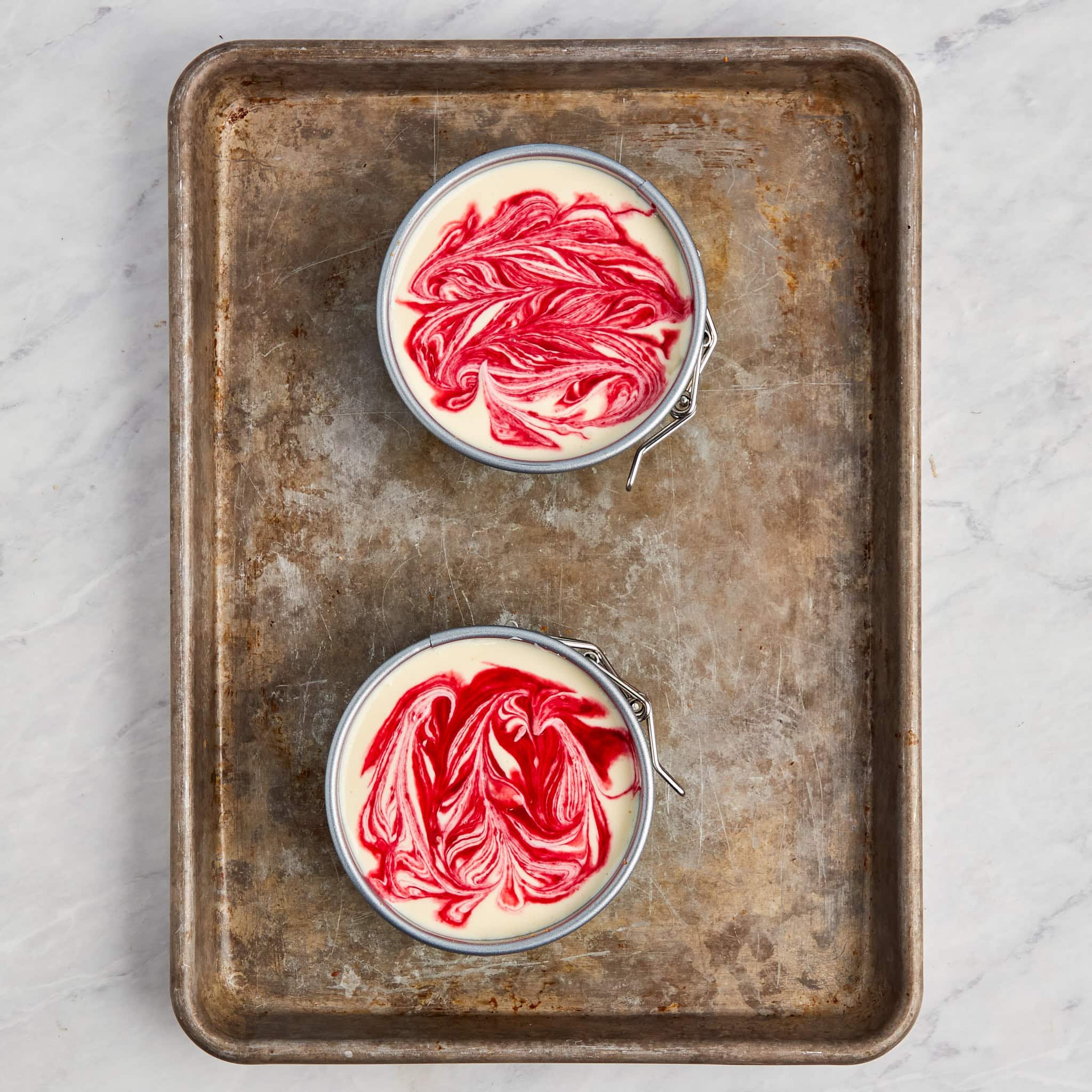 two 6-inch unbacked raspberry cheesecakes in springform pans on a cookie sheet.