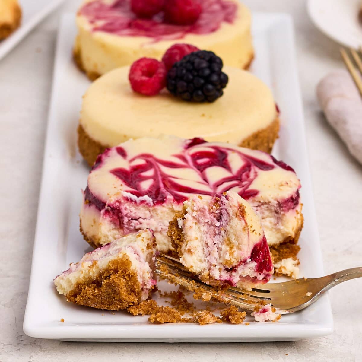 fork and pieces of raspberry cheesecake cut from a small cheesecake on a white plate.