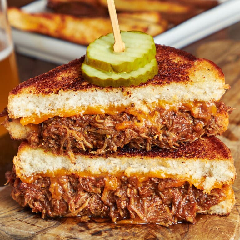 BBQ pulled pork grilled cheese cut in half, stacked and served on a wooden board.
