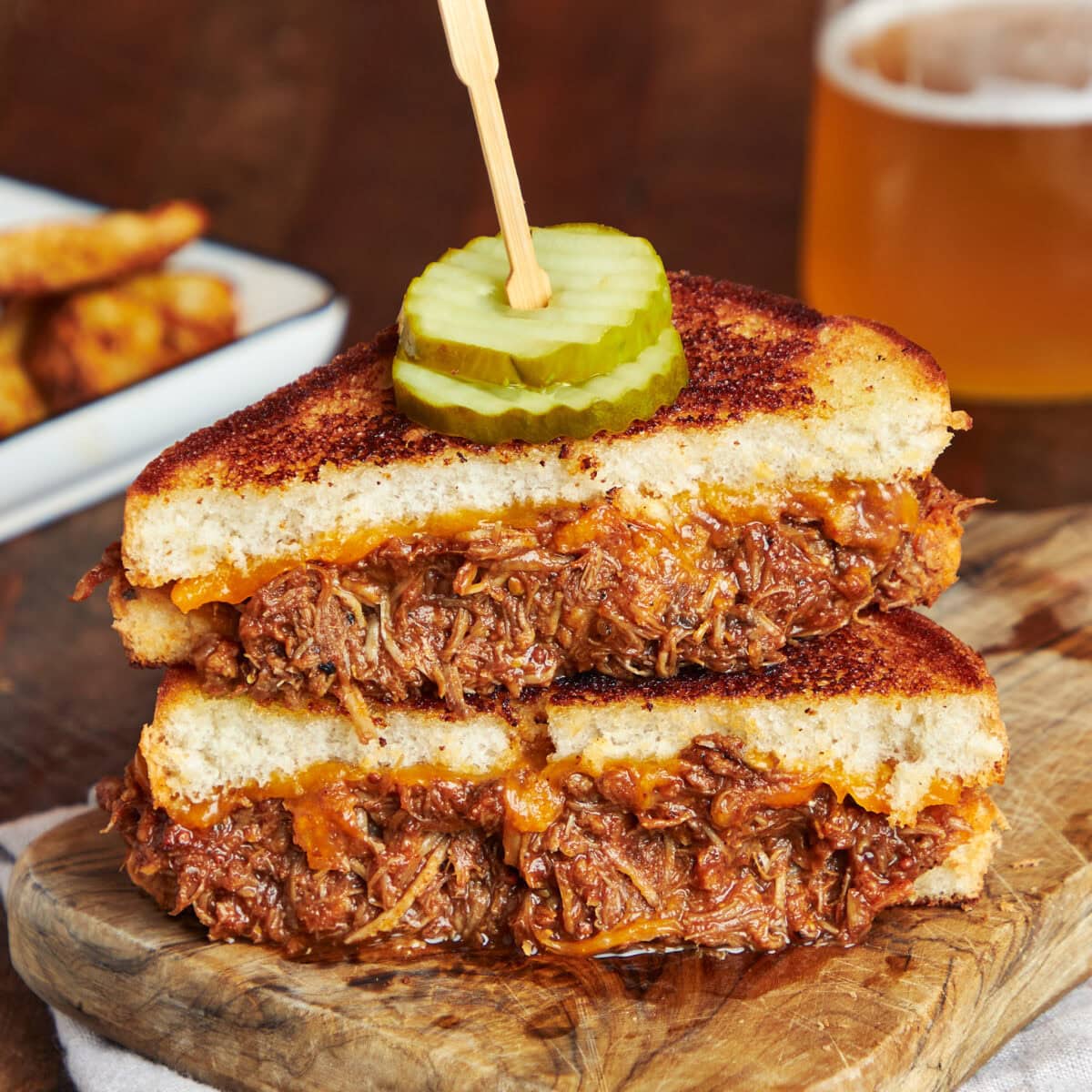 BBQ pulled pork grilled cheese cut in half, stacked and served on a wooden board.